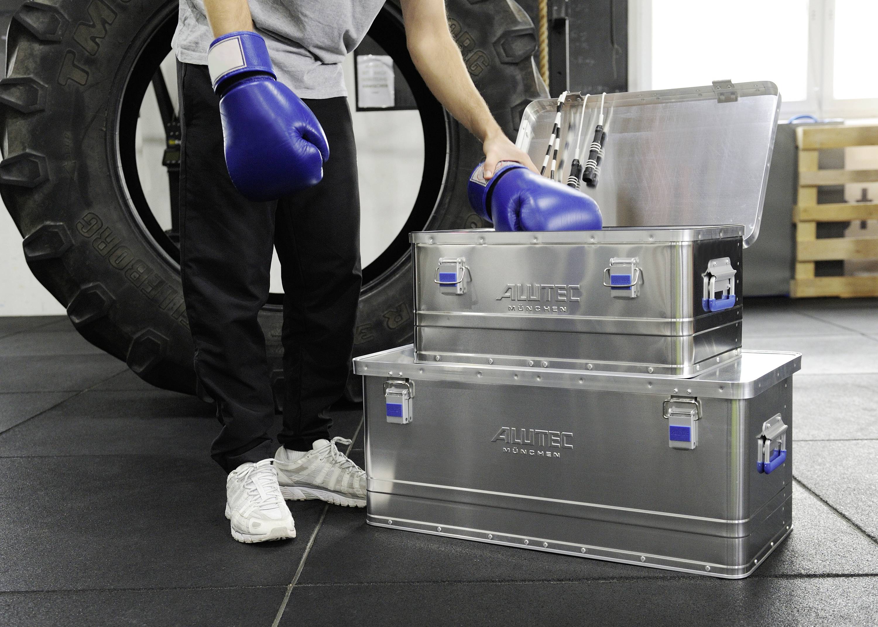 Person mit blauen Boxhandschuhen zieht einen aus Metallkisten im Fitnessstudio.
