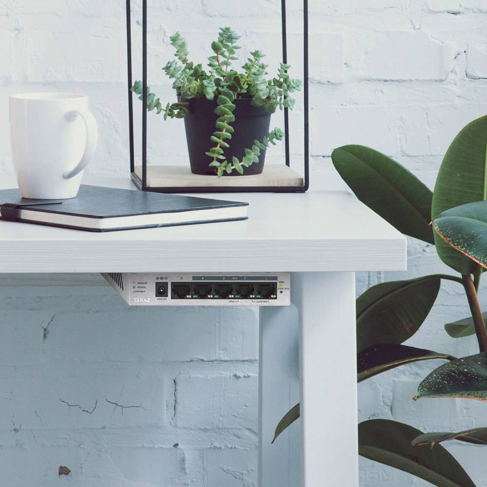 Ein weißer Tisch mit einer Tasse, einem Notizbuch und einem Topf mit Sukkulenten. Darunter ist ein Netzwerkgerät an der Tischkante montiert.