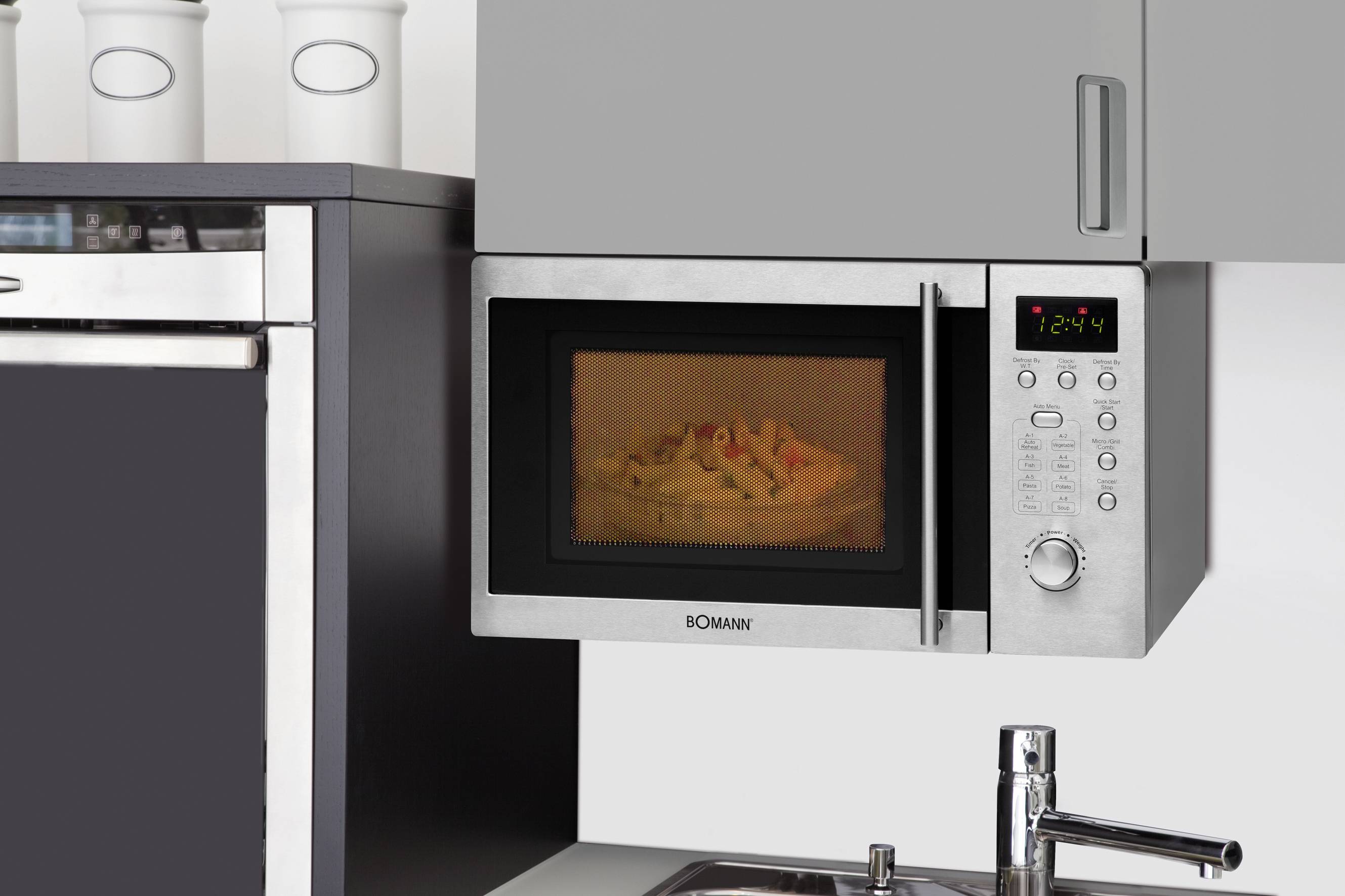 Eine Mikrowelle in moderner Küche wärmt einen Teller mit Essen. Neben der Mikrowelle stehen weiße Vorratsdosen auf dem Regal.