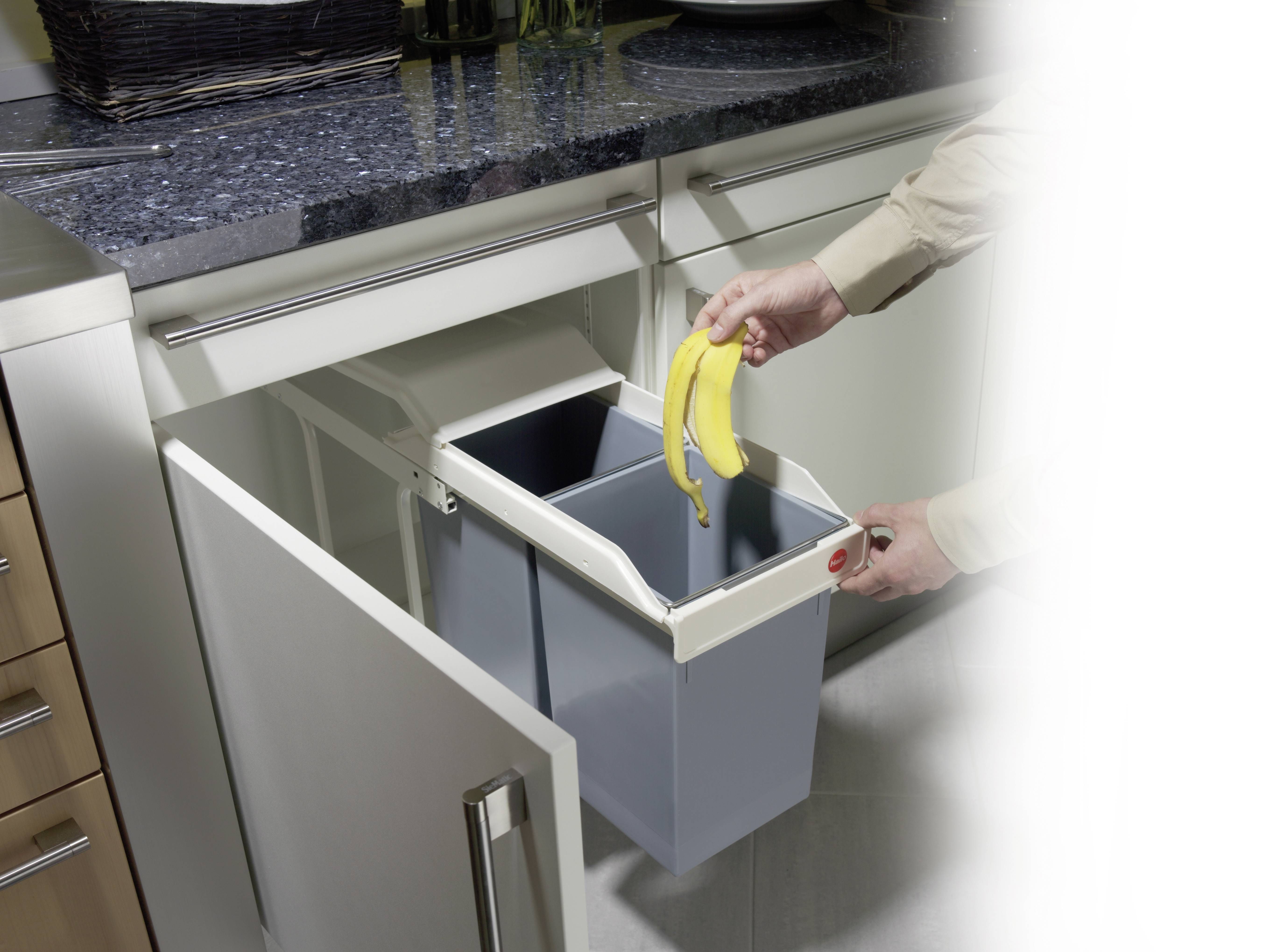 Eine Person wirft eine Bananenschale in einen ausziehbaren Abfalleimer in einer Küche unter der Arbeitsplatte.