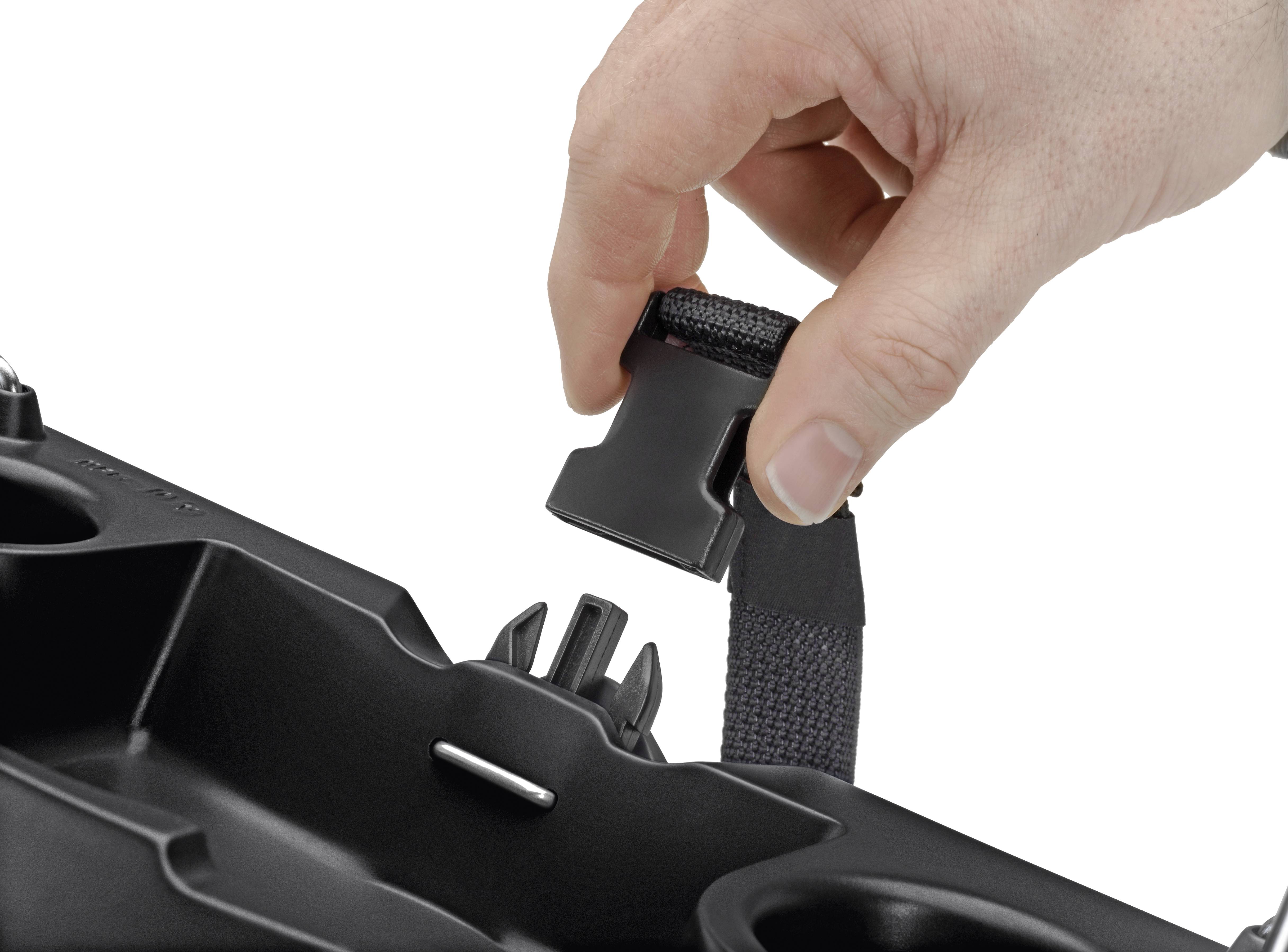 Eine Hand hält einen Sicherheitsgurtclip über einer schwarzen Autositzeinlage mit Getränkehaltern und Halterungen.