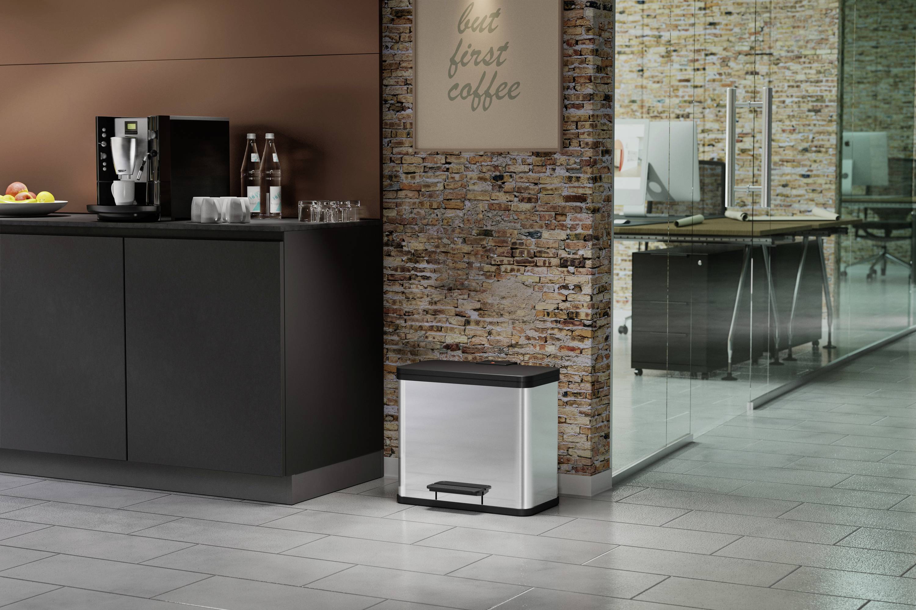 Küche mit Kaffeemaschine auf einem schwarzen Schrank; daneben steht ein silberner Mülleimer. Im Hintergrund ein Glasbüro.