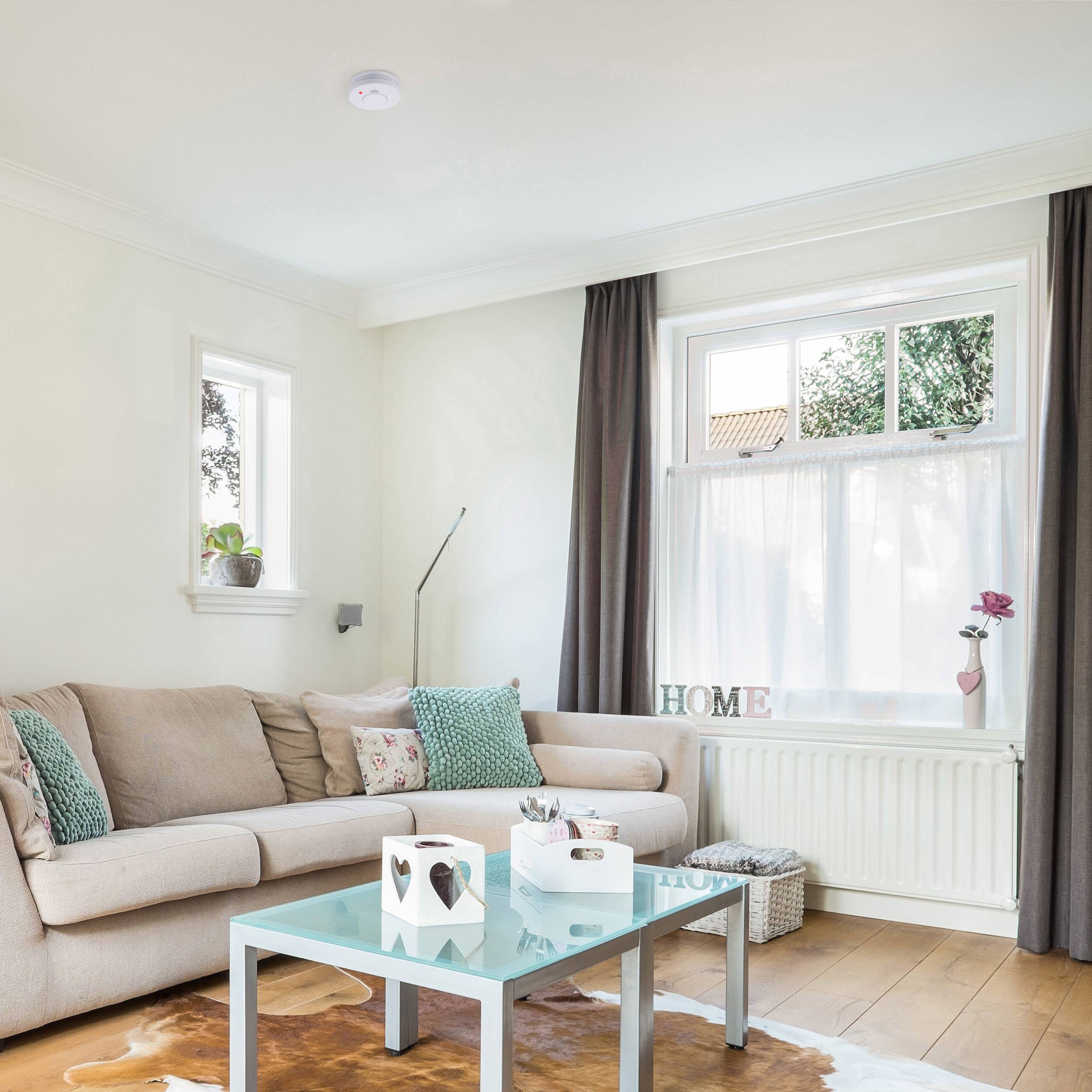 Helles Wohnzimmer mit beiger Couch, blauen Kissen, grauen Vorhängen und einem Kaffeetisch; Fenster mit 'HOME'-Dekoration.