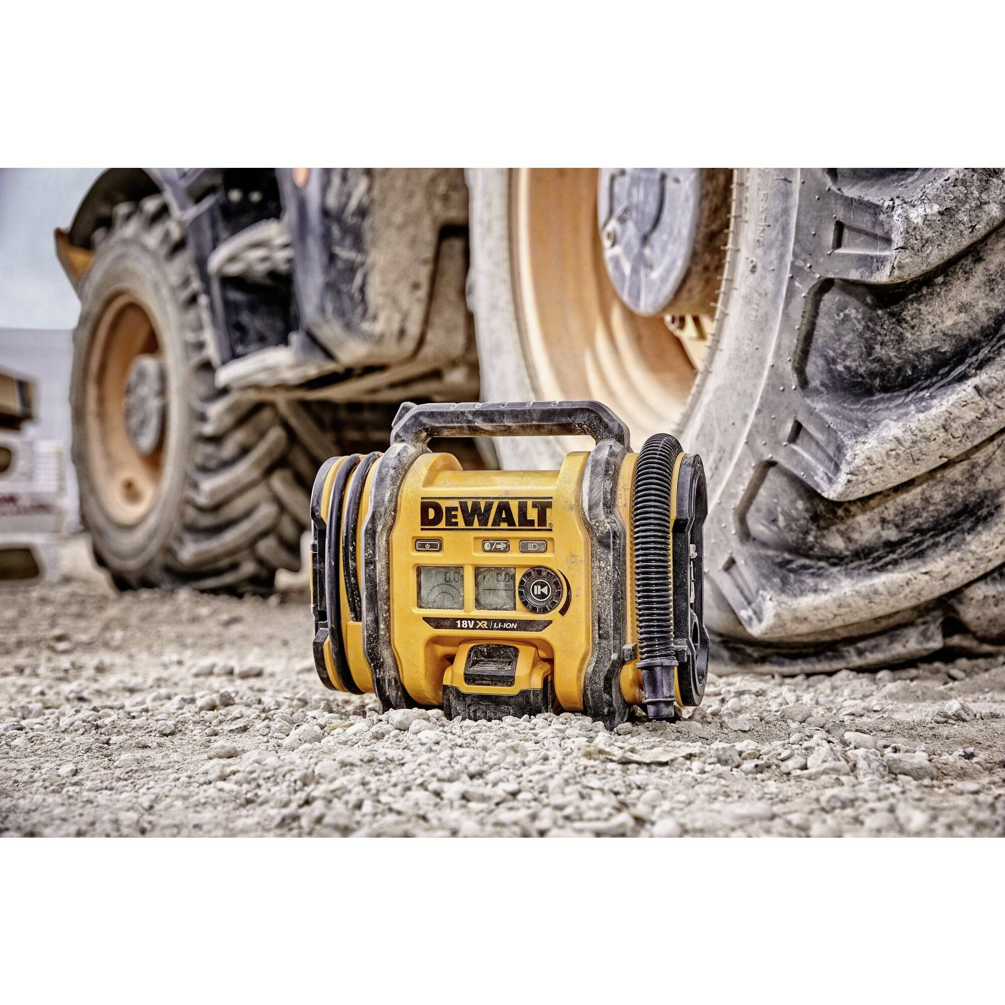 Ein gelber Baustellenradio der Marke DeWalt steht auf sandigem Boden vor einem großen Traktorrad.