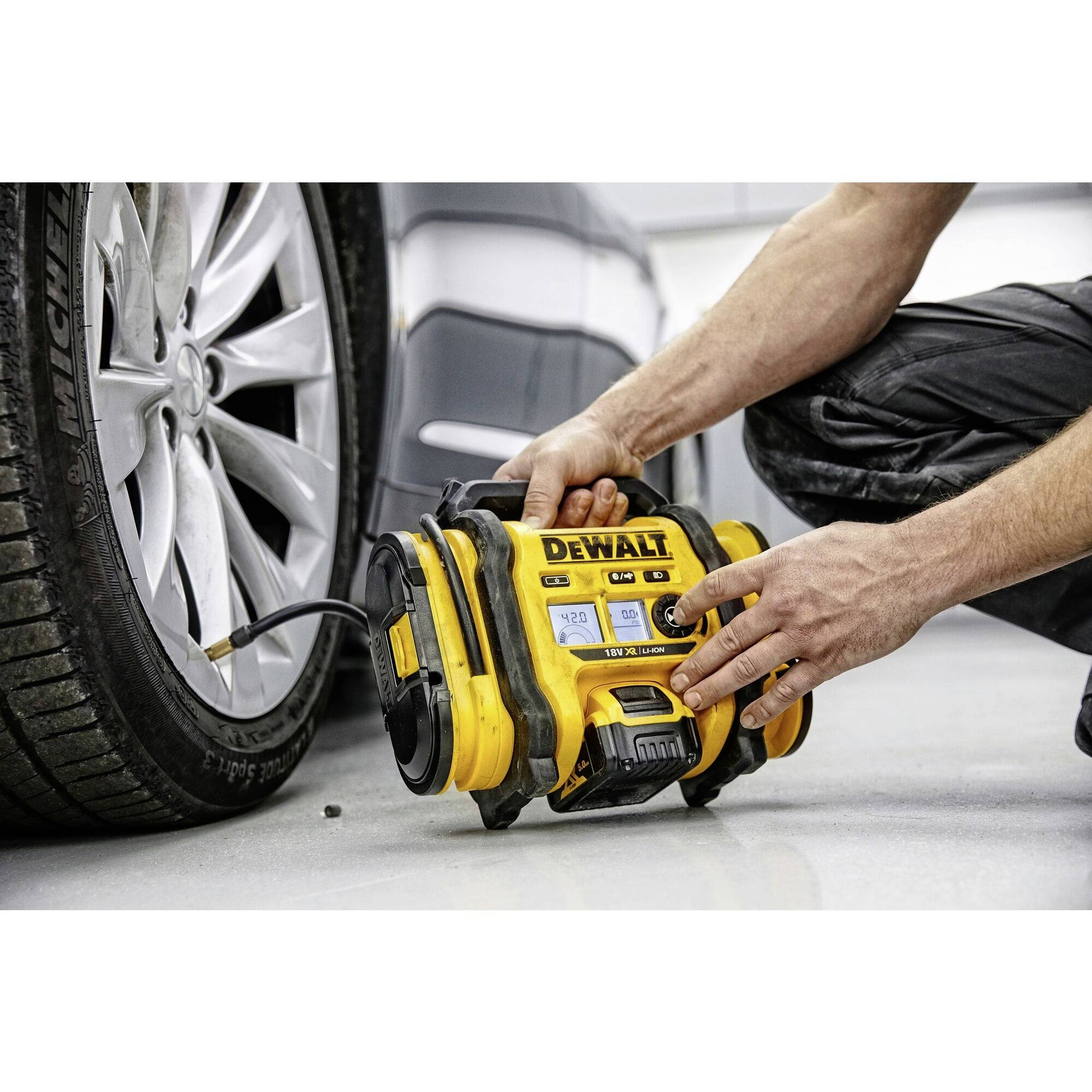 Eine Person pumpt mit einem gelben, tragbaren Luftkompressor einen Autoreifen auf. Der Kompressor zeigt '20 PSI' auf dem Display.