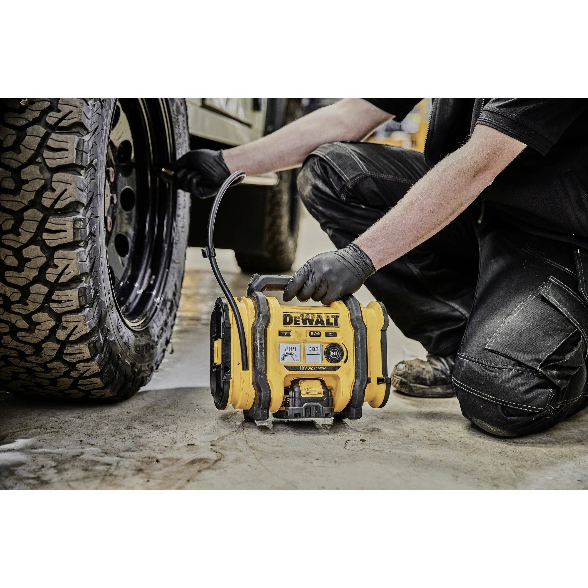 Mann pumpt Autoreifen mit tragbarem Luftkompressor von DeWalt auf, trägt schwarze Hose und Handschuhe, im Freien.