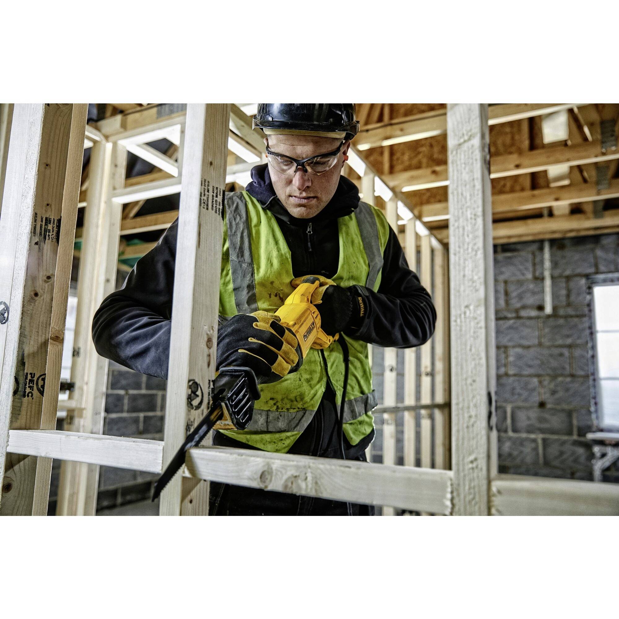 Eine Person in Schutzkleidung und Helm benutzt eine Säge, um Holz in einem im Bau befindlichen Gebäude zu schneiden.