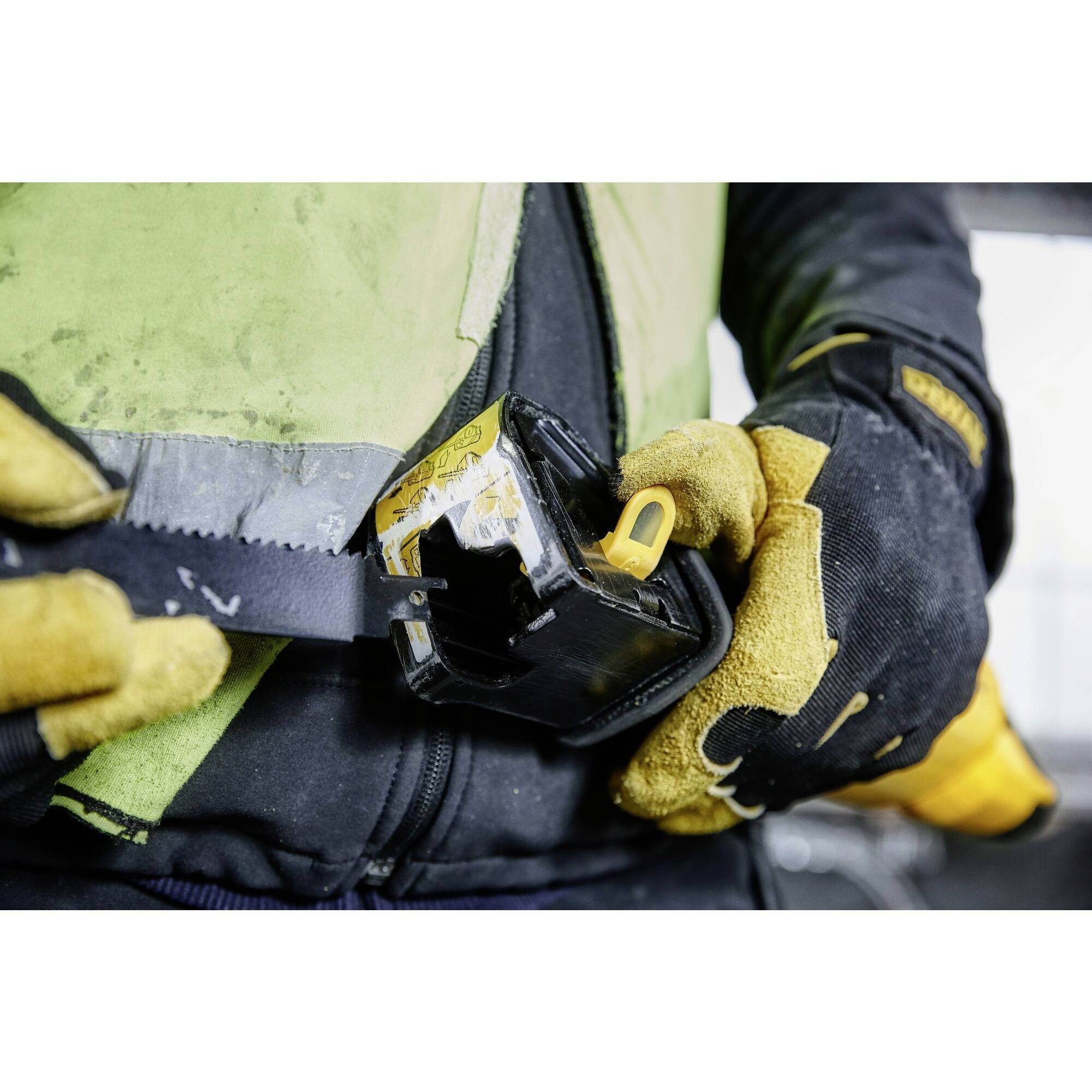 Arbeiter mit gelbem Handschuh zieht Bandmaß aus schwarzer Hülle. Szene zeigt praktische Anwendung eines Werkzeuges.
