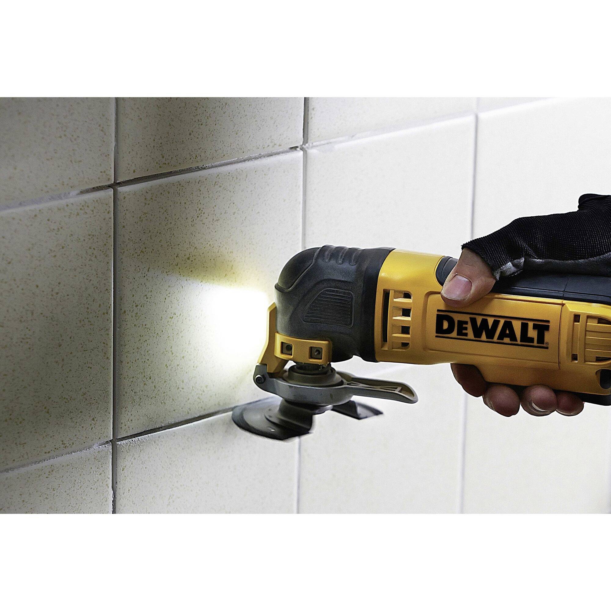 Eine Person verwendet ein Multifunktionswerkzeug auf einer Fliese. Das Werkzeug hat eine Lampe und wird für präzise Arbeiten eingesetzt.