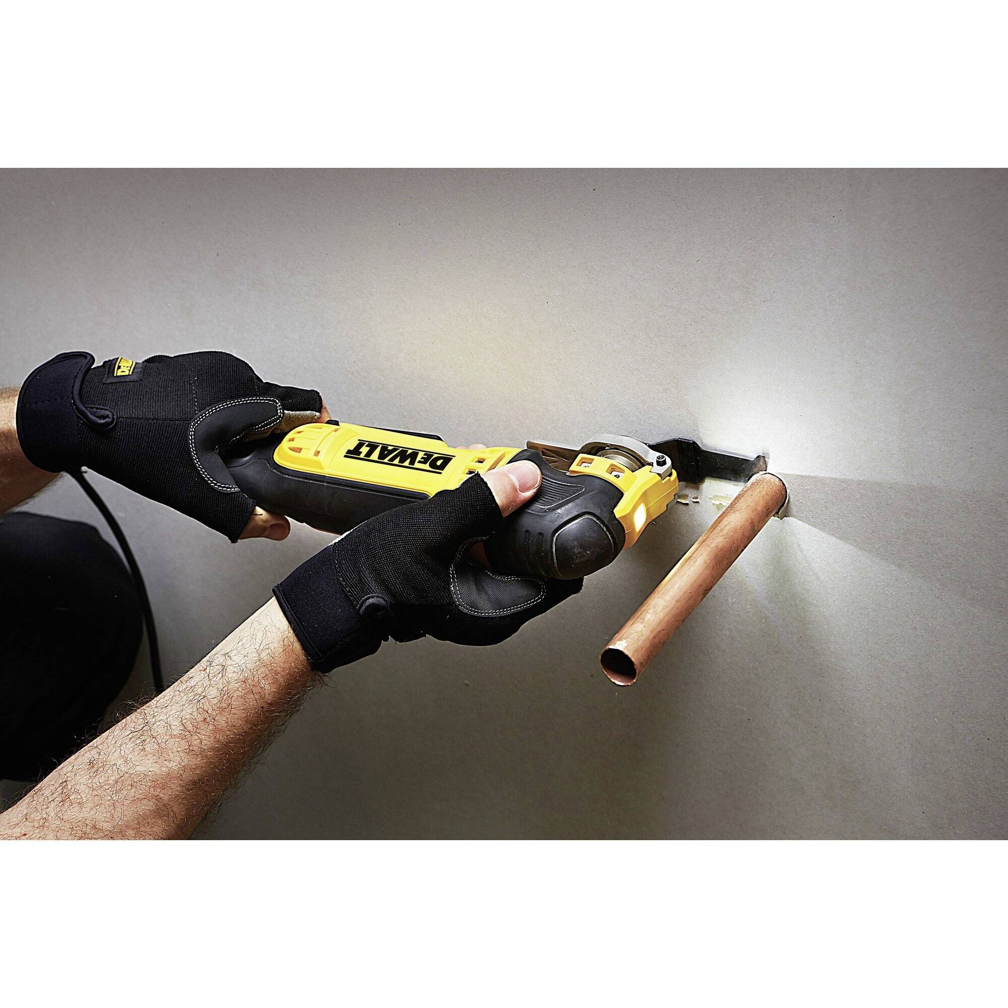 Eine Person schneidet mit einem elektrischen Werkzeug ein Kupferrohr an einer Wand. Die Person trägt schwarze Handschuhe.