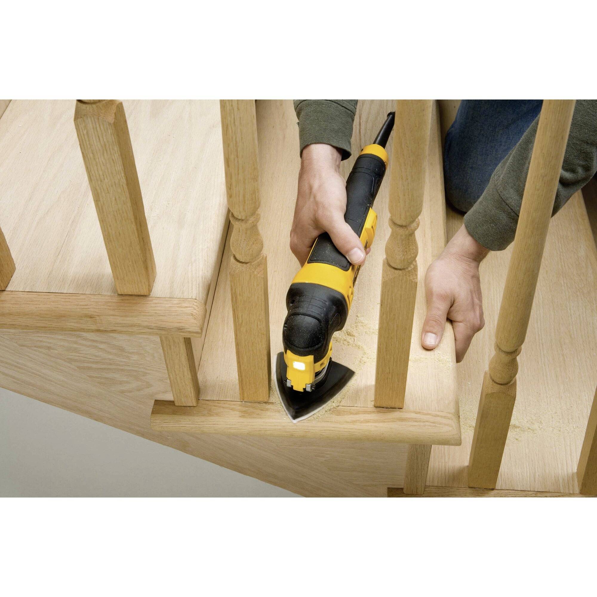 Eine Person schleift mit einem Elektrowerkzeug die Ecken einer Holztreppe ab. Holzspäne sind sichtbar.