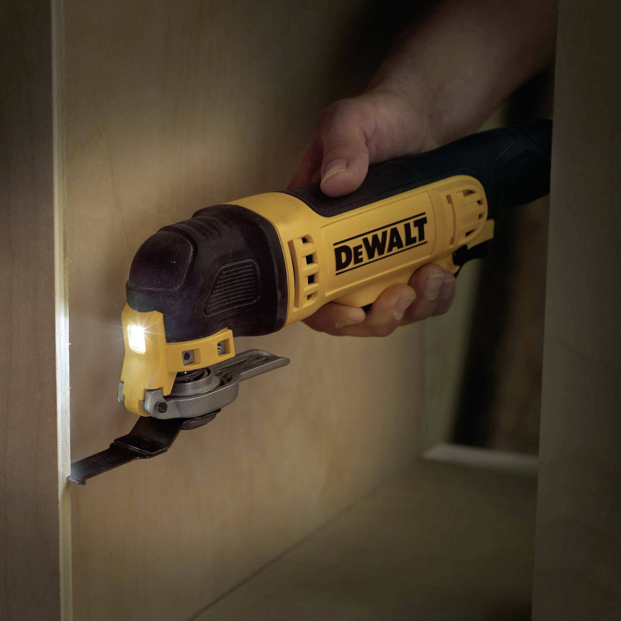 Eine Person benutzt ein elektrisches Multifunktionswerkzeug der Marke DeWalt in einem Innenraum. Das Werkzeug hat eine Beleuchtung.