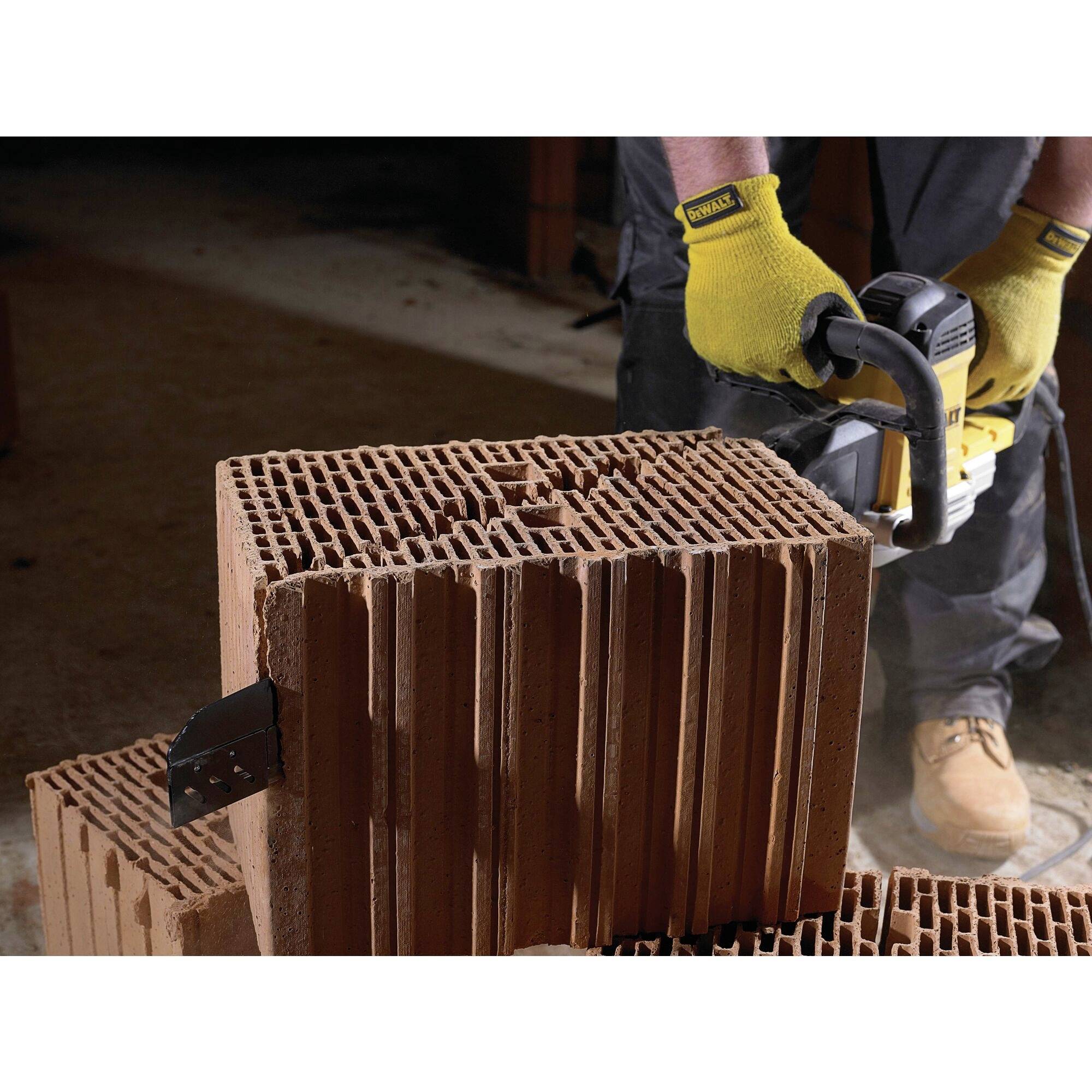 Person in Arbeitshandschuhen durchtrennt mit einer Kettensäge einen porösen Ziegelstein. Staub und Splitter fliegen ab.