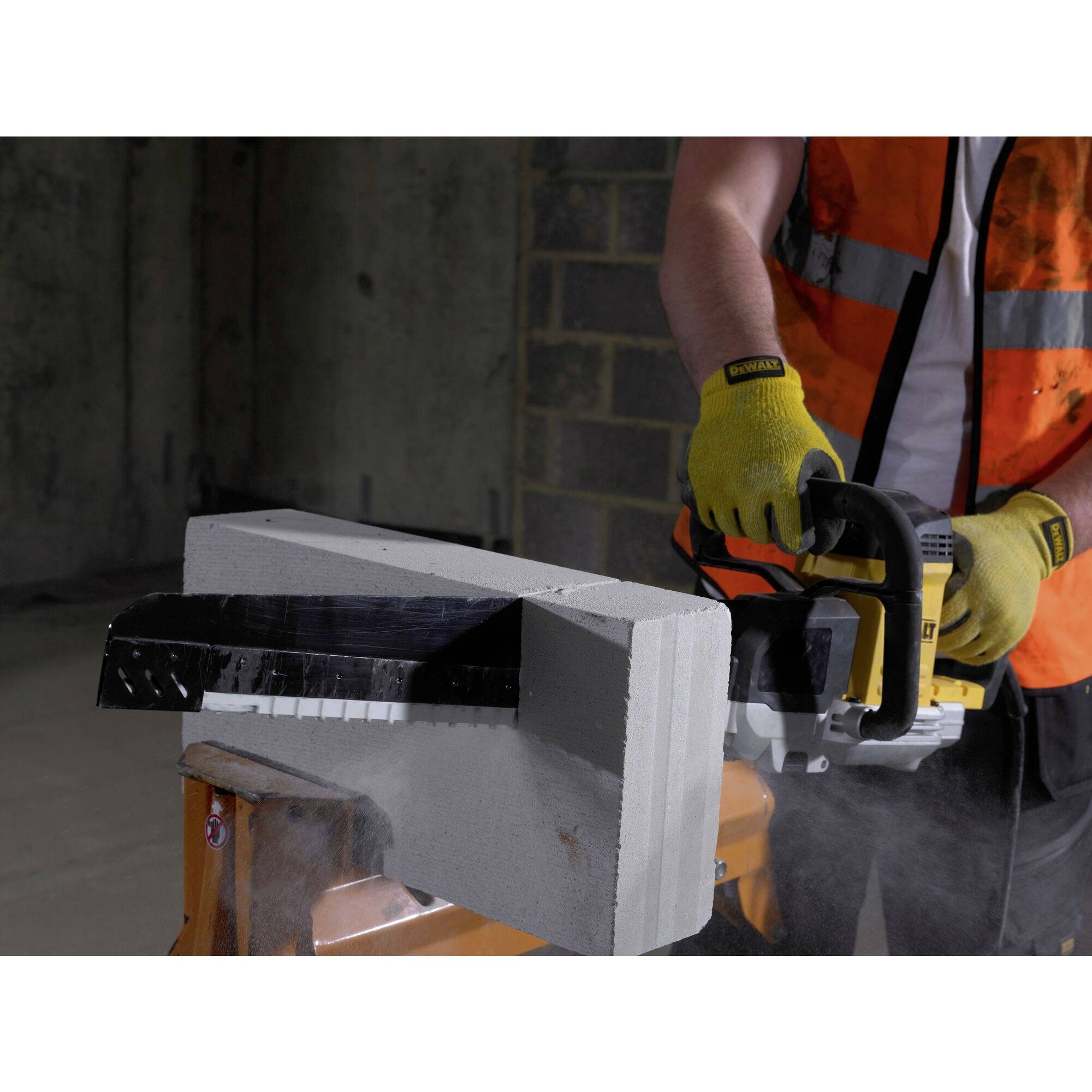 Eine Person in Sicherheitskleidung schneidet mit einer Elektrosäge einen großen Betonblock in einer Baustellenumgebung.