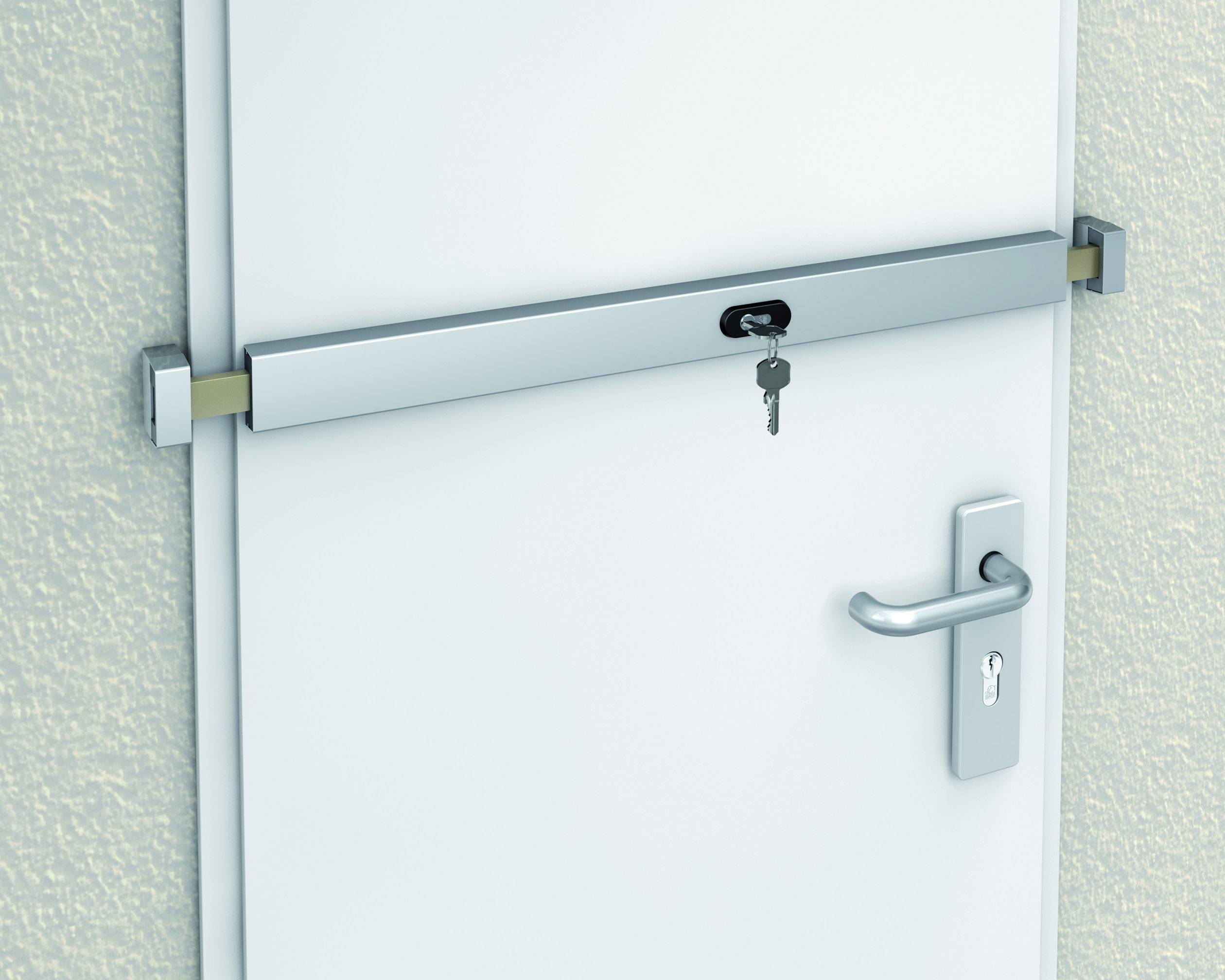 Silberne Sicherheitsstange an einer weißen Tür mit einem Schlüssel im Schloss. Die Türklinke befindet sich rechts.