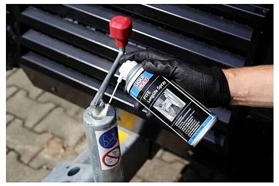 Eine Person in einem schwarzen Handschuh sprüht PTFE-Langzeitspray auf den Kopplungsbereich der Maschine auf und verbessert so die Schmierung und reduziert die Reibung.