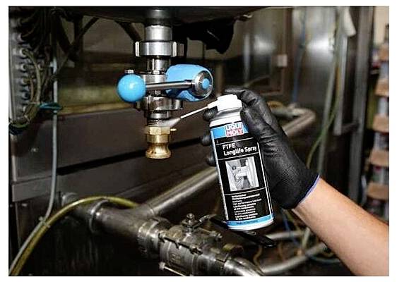 Person in Handschuh sprüht Schmiermittel auf einen Metallhahn, möglicherweise zur Wartung.