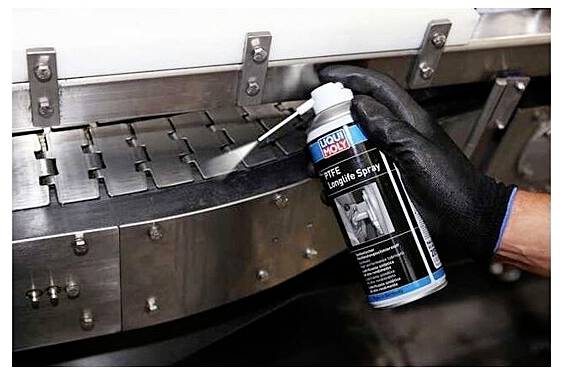 Behandschuhte Hand sprüht Schmiermittel auf ein Metallförderband und zeigt Wartungsarbeiten an Industrieanlagen.