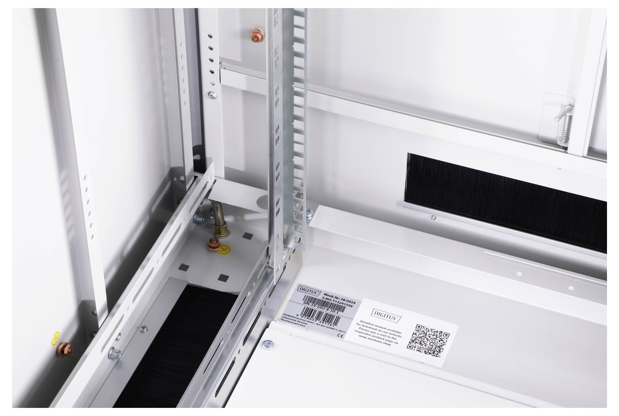 Innenansicht eines weißen Geräteschrankes mit Metallrahmen und einem QR-Code auf einer Oberfläche. Kabelöffnungen und Befestigungselemente sichtbar.