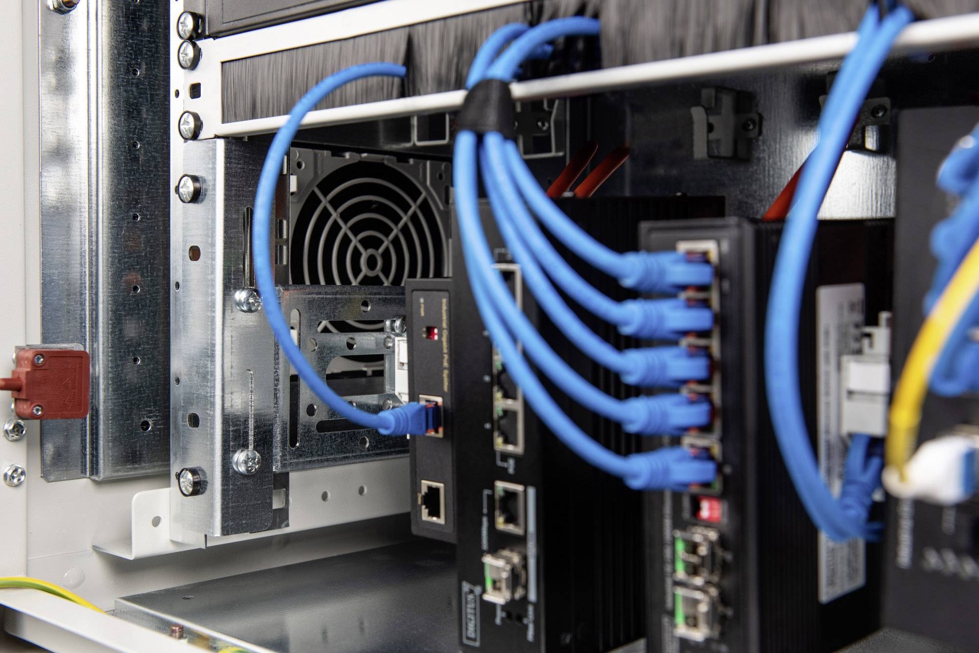 Serverraum mit mehreren angeschlossenen Netzwerkkabeln und Hardwarekomponenten. Ventilator sichtbar im Hintergrund.