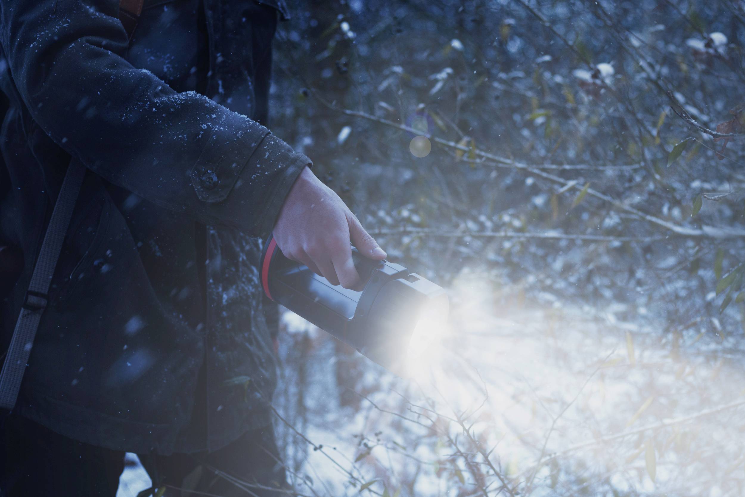 Eine Person hält eine leuchtende Taschenlampe in einem verschneiten Wald, während Schneeflocken fallen.
