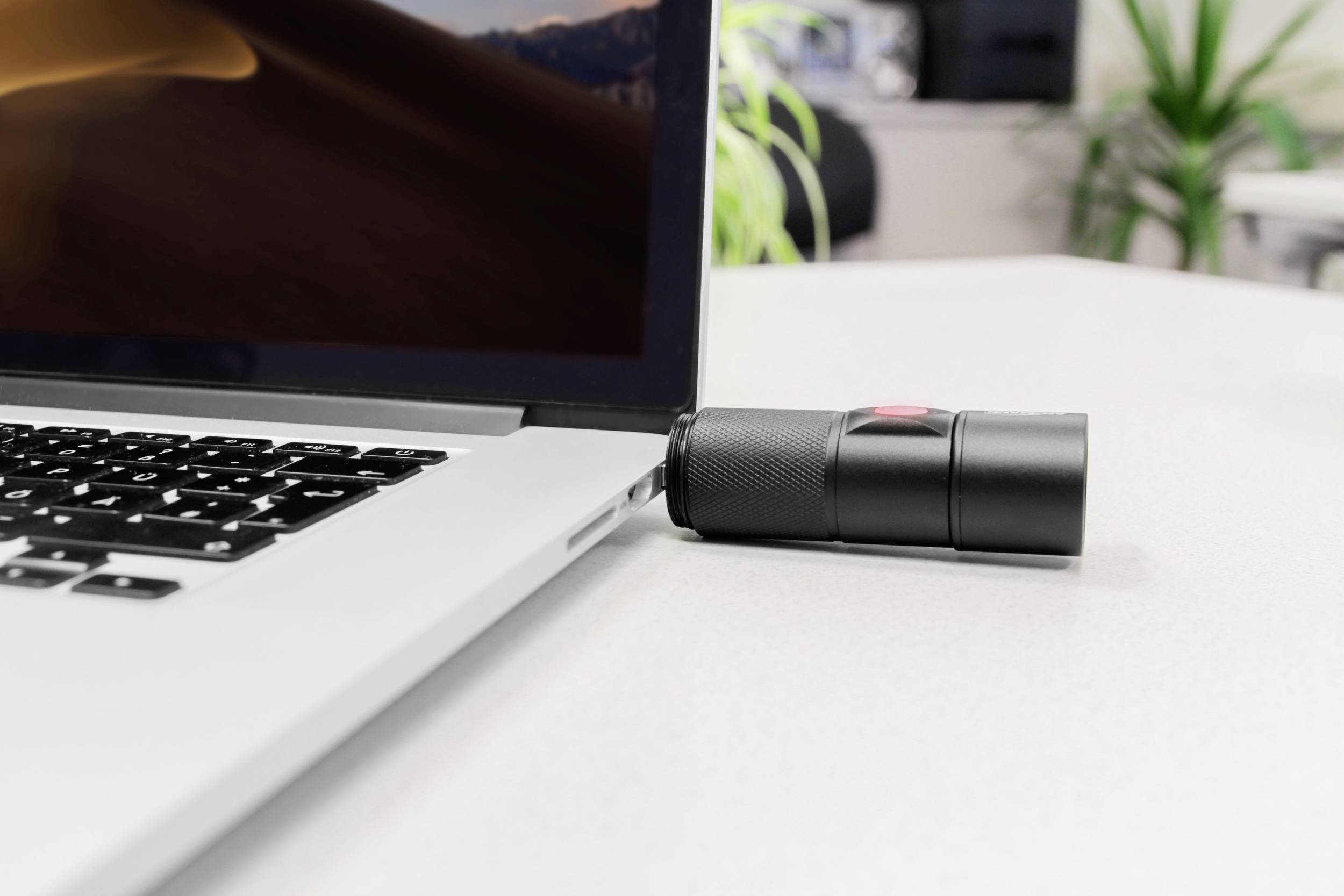Ein Laptop steht auf einem Tisch. Ein kleiner, schwarzer Lautsprecher oder ein ähnliches Gerät lehnt an der rechten Seite des Laptops.