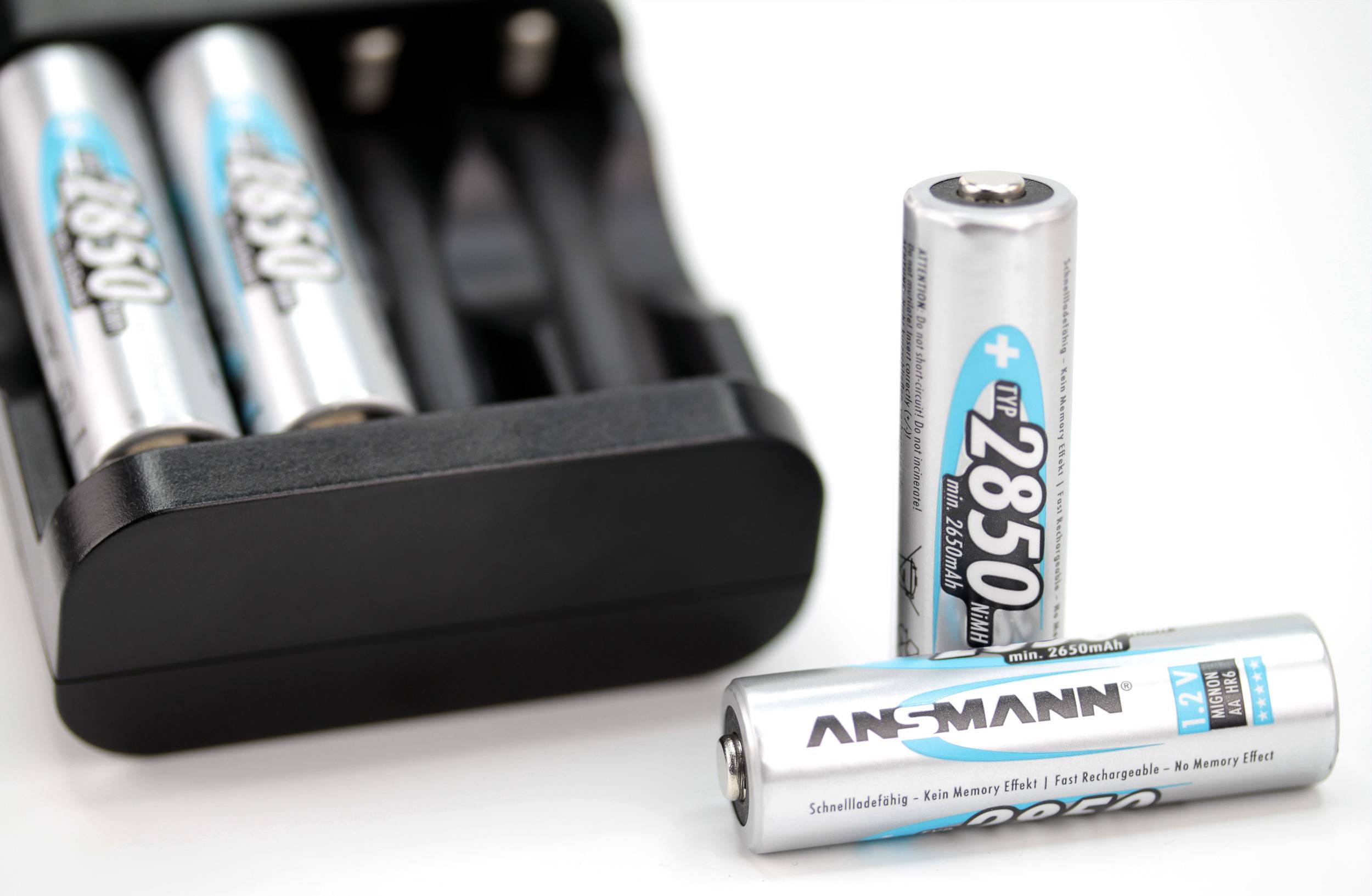 Nahaufnahme von zwei wiederaufladbaren AA-Batterien der Marke Ansmann und einem Ladegerät im Hintergrund.