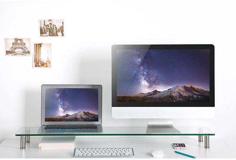 Ein Laptop und ein Desktop-Computer auf einem Schreibtisch zeigen dasselbe Sternenhimmelbild. Im Hintergrund sind Fotos an der Wand.