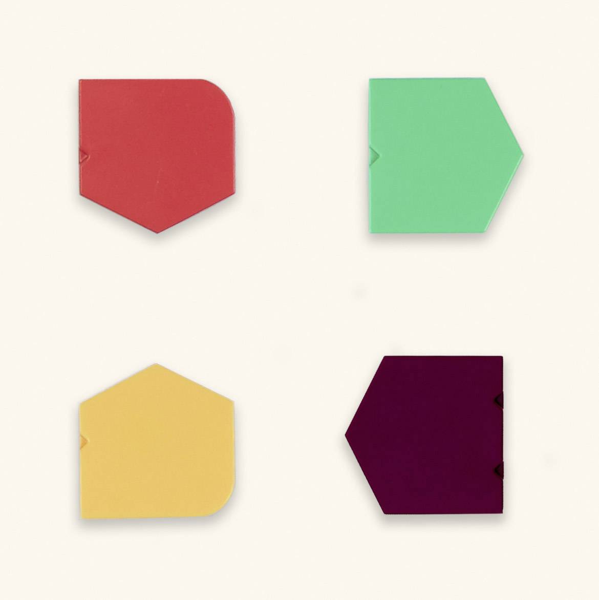 Vier bunte, geometrische Formen: ein rotes Fünfeck, ein grünes Sechseck, ein gelbes Fünfeck und ein violettes Sechseck, auf beigem Hintergrund.