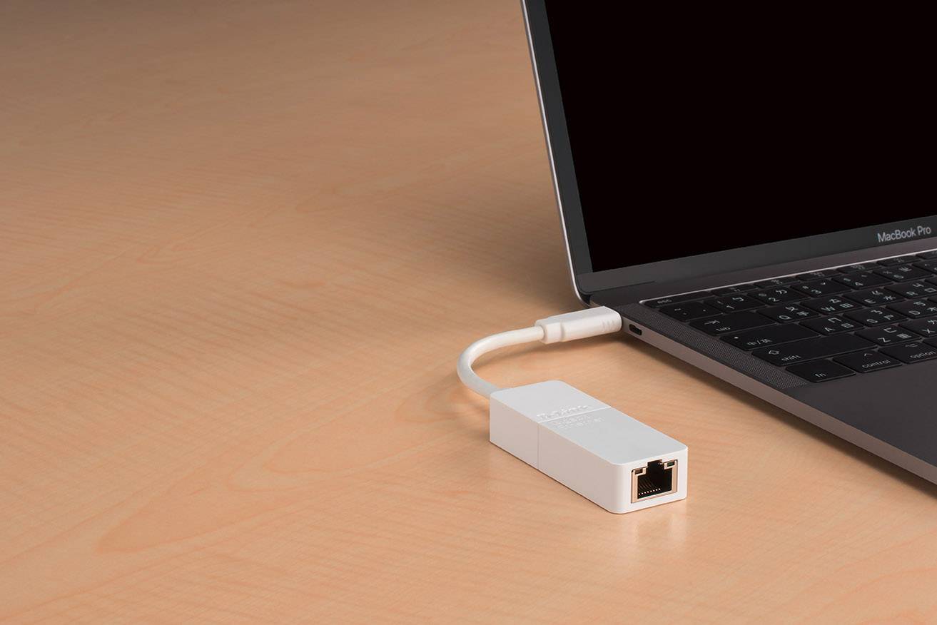 Ein weißer Ethernet-Adapter ist an einen schwarzen Laptop angeschlossen, der auf einem Holztisch steht.