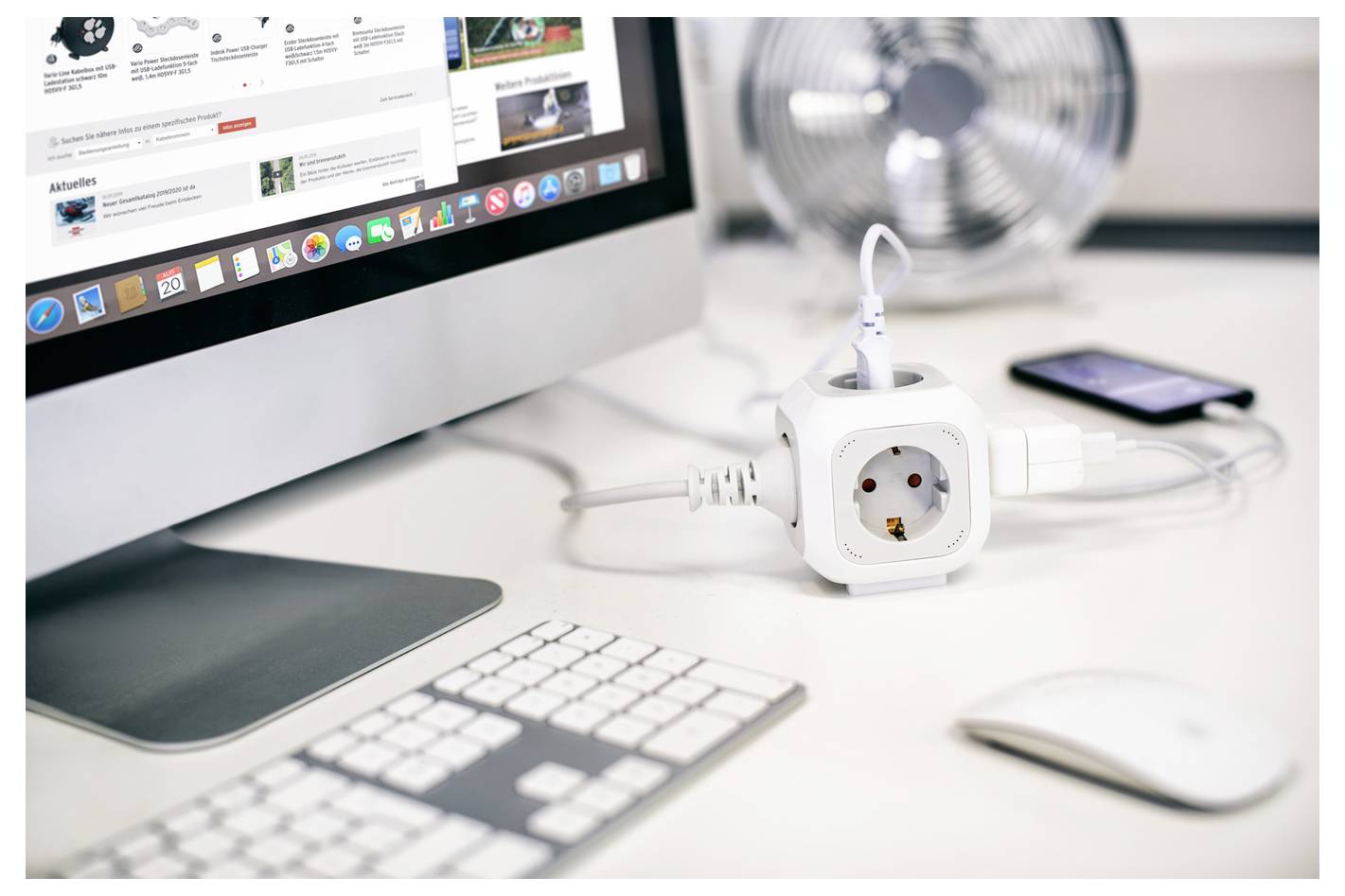 Desktop-Arbeitsplatz mit iMac, Tastatur, Maus, Netzteil, Ventilator und Smartphone auf weißem Schreibtisch