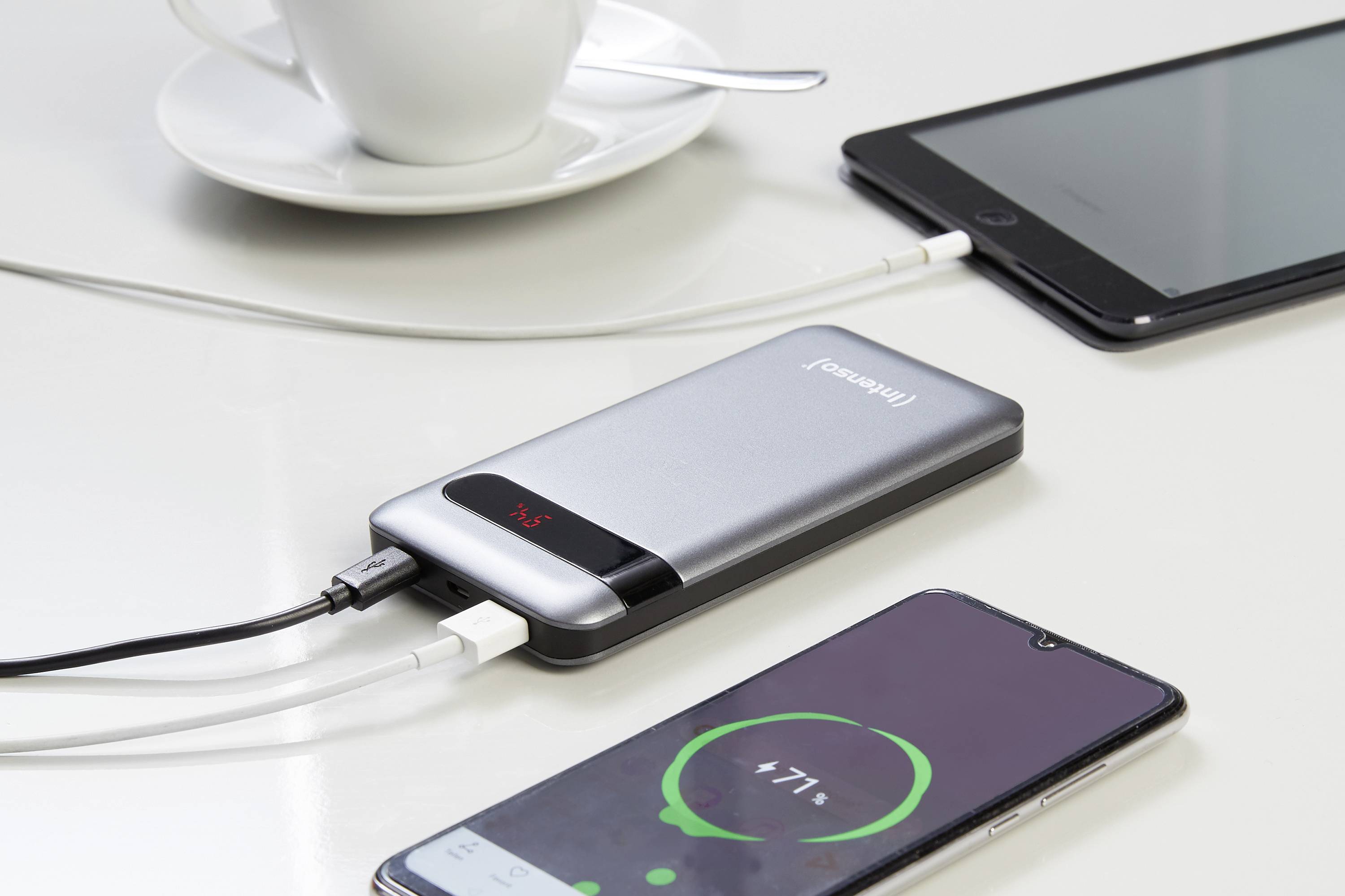 Eine Powerbank mit der Aufschrift 'Intenso' lädt zwei Smartphones gleichzeitig. Beide Displays zeigen den Ladevorgang an.