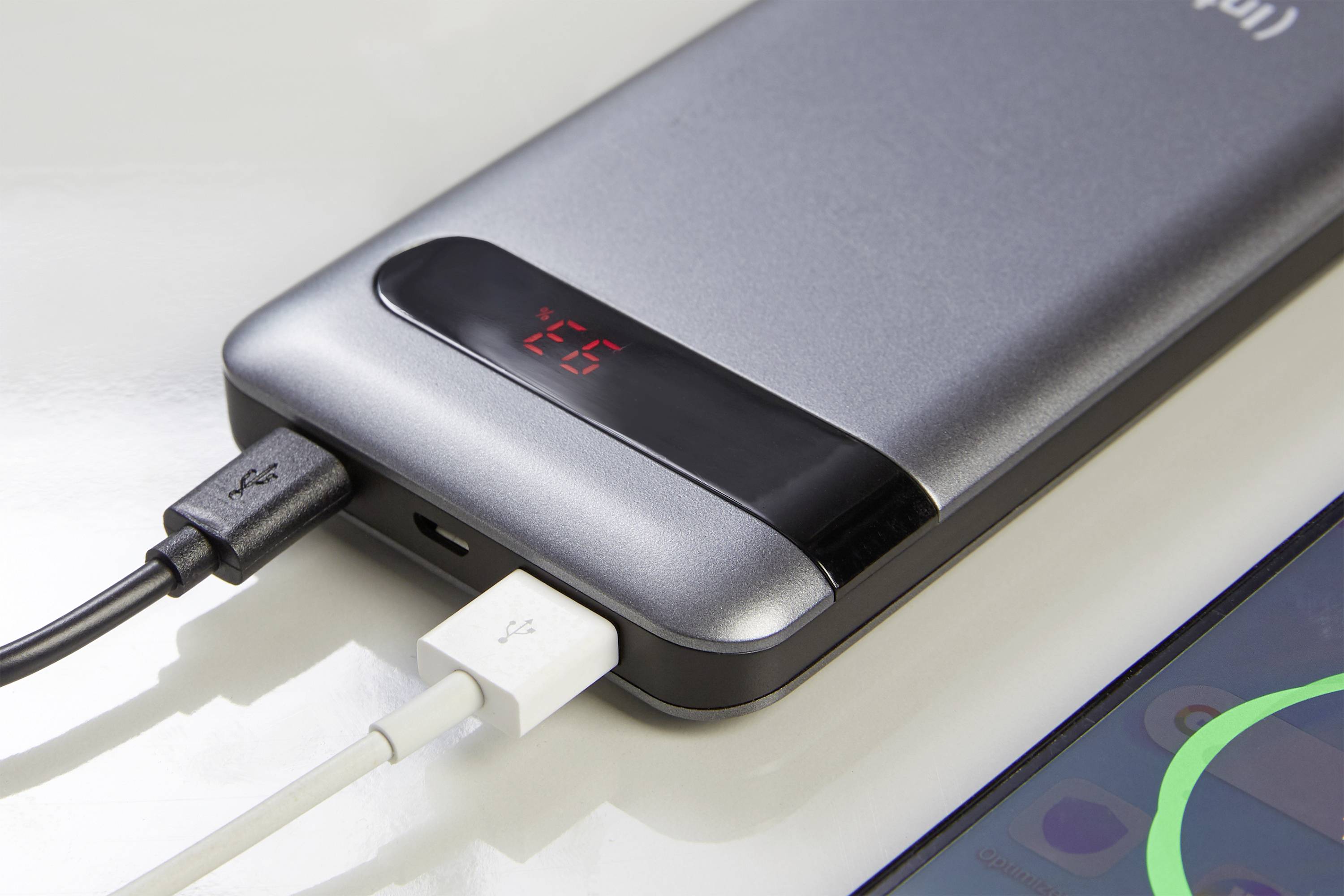 Eine silberne Powerbank zeigt die Zahl 25 auf einem digitalen Display und lädt ein Gerät über zwei angeschlossene Kabel auf.