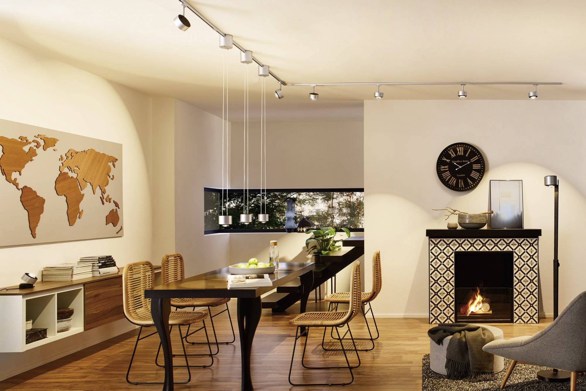 Ein gemütlicher Essbereich mit Holztisch und Stühlen, einer Weltkarte an der Wand, einem Kamin und Fenstern mit Blick ins Freie.