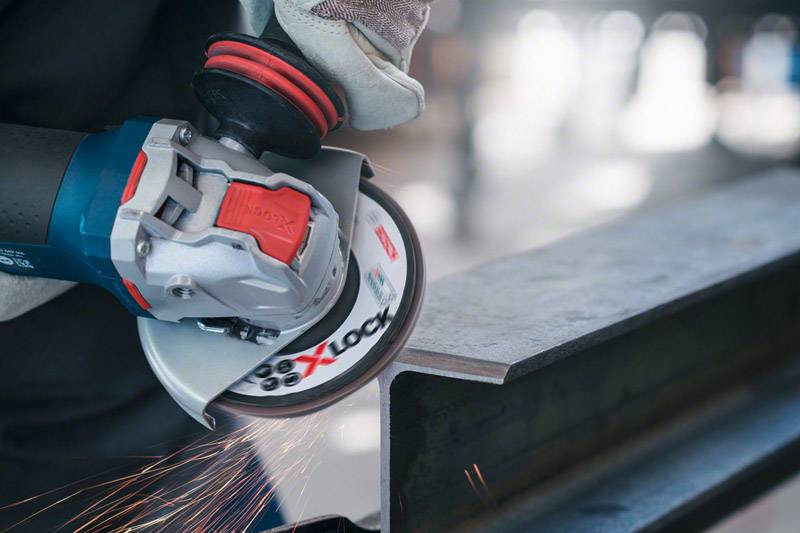 Eine Person schleift mit einem Winkelschleifer Metall. Funken fliegen vom Kontaktpunkt, was auf aktive Bearbeitung hinweist.