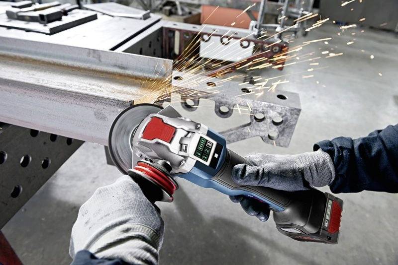 Ein Handwerker schleift Metall mit einem Winkelschleifer. Funken fliegen umher. Der Arbeitsplatz ist industriell und funktional eingerichtet.