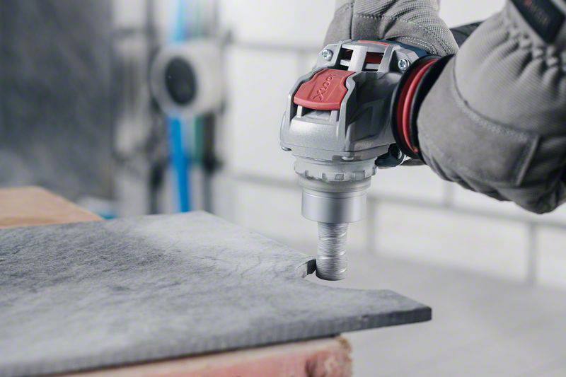 Ein Arbeiter mit grauem Handschuh schneidet mit einem elektrischen Werkzeug durch ein graues, flaches Material, wie Metall oder Stein.