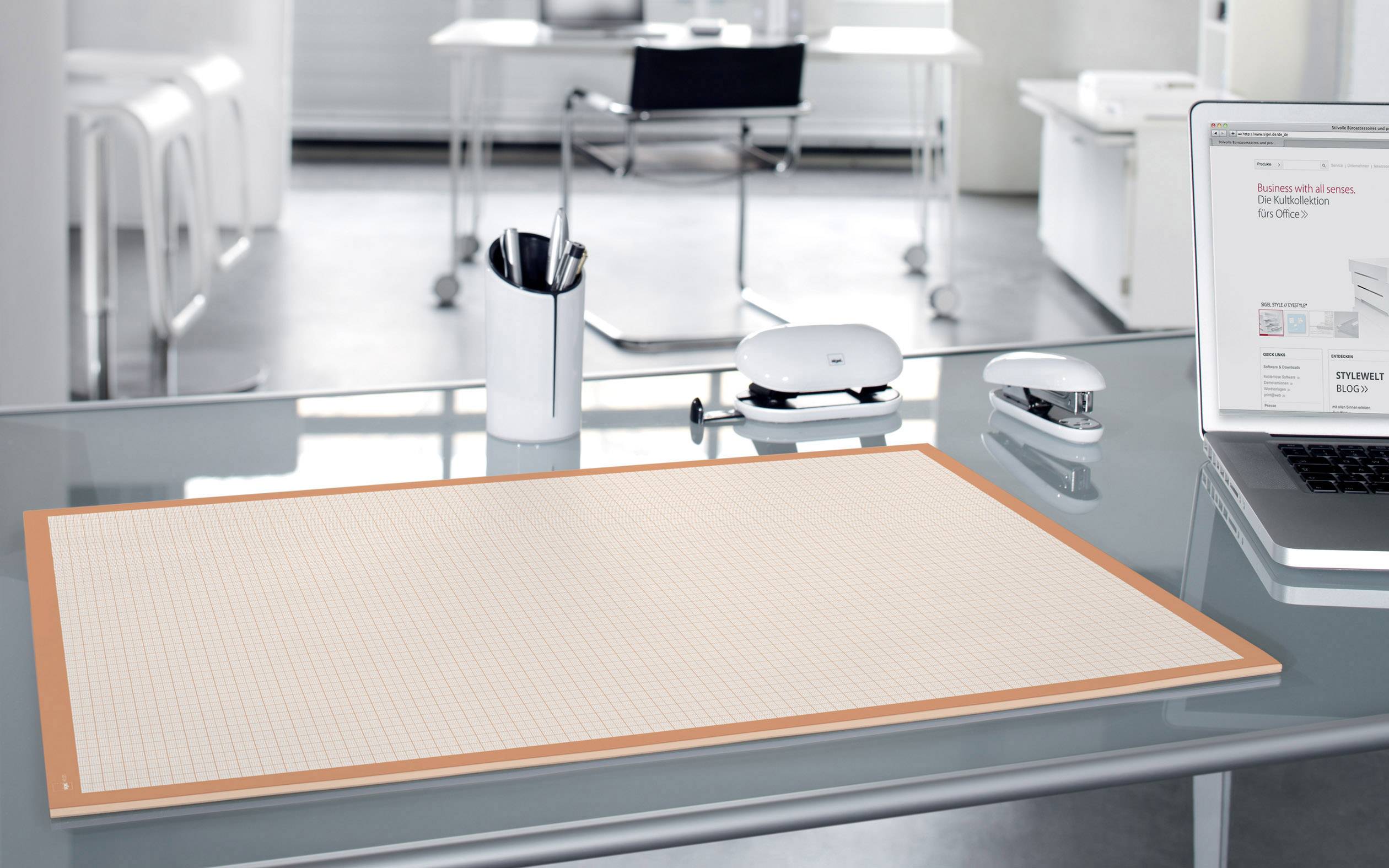 Modernes Büro mit Glas-Schreibtisch, Notizblock, Laptop, Maus und Stiftehalter. Der Raum ist offen und minimalistisch gestaltet.