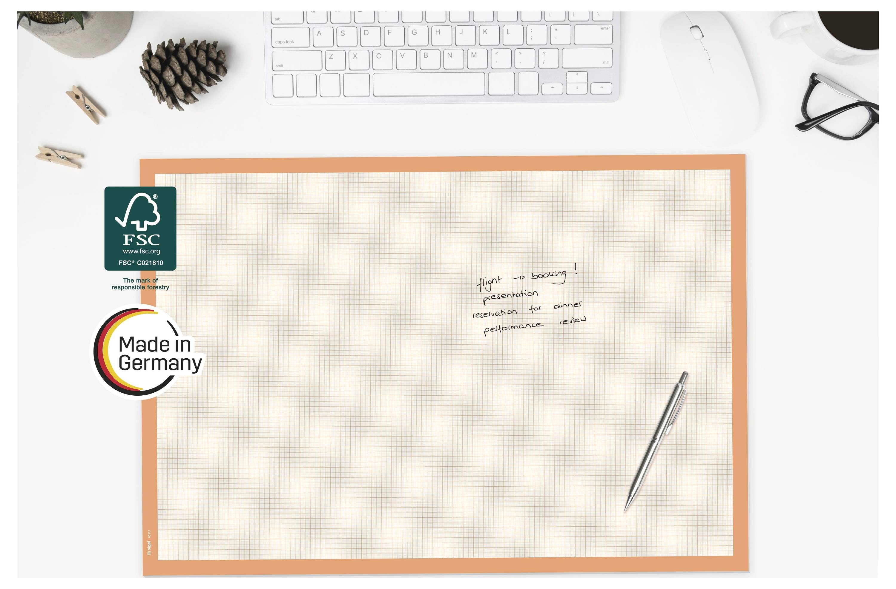 Leeres Millimeterpapier-Notizbuch auf einem weißen Schreibtisch, mit einem Stift, Tastatur, Brille und FSC- sowie „Made in Germany"-Etiketten auf der linken Seite.