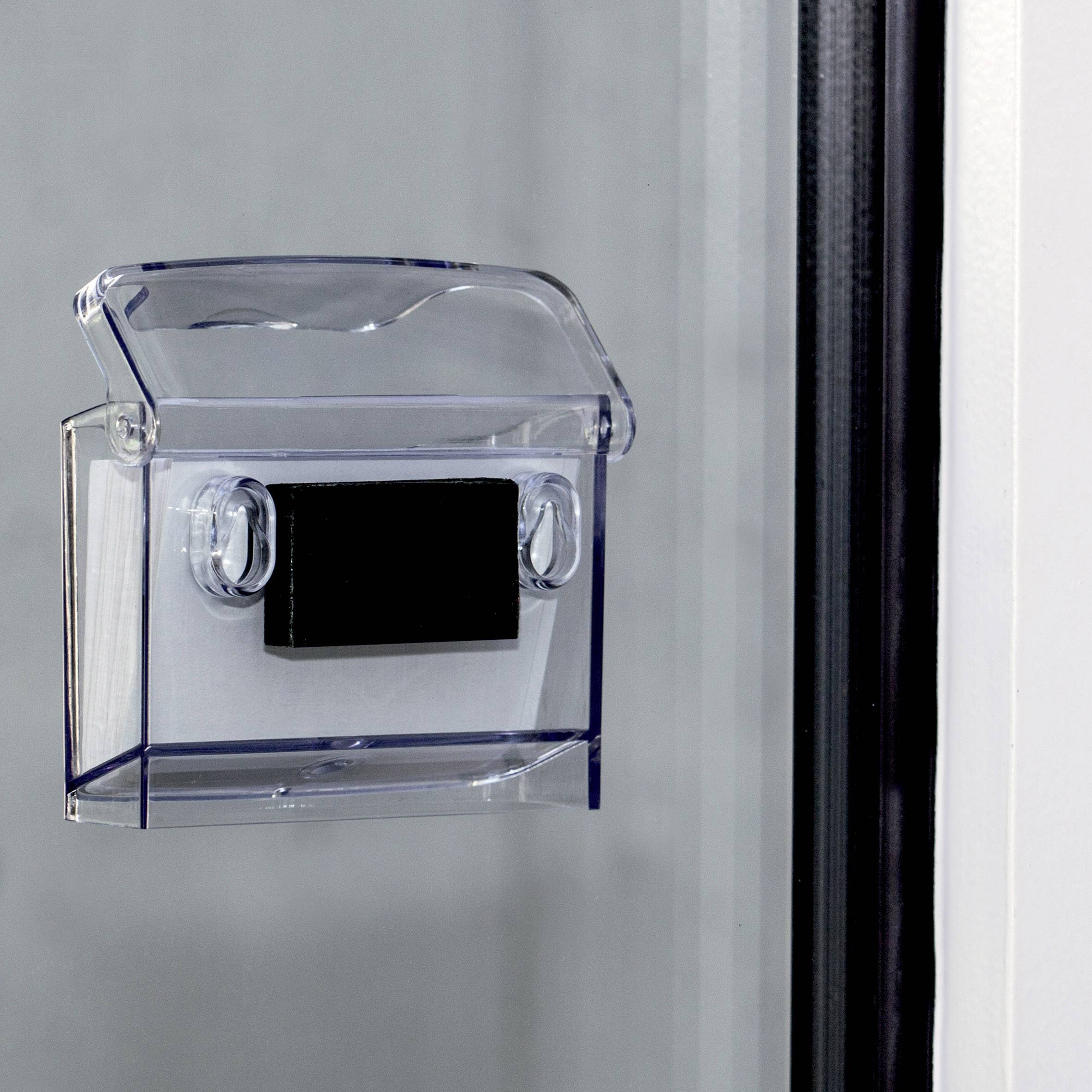 Transparenter Behälter mit schwarzem Rechteck an Glaswand befestigt, vermutlich für Karten- oder Dokumentenaufbewahrung.