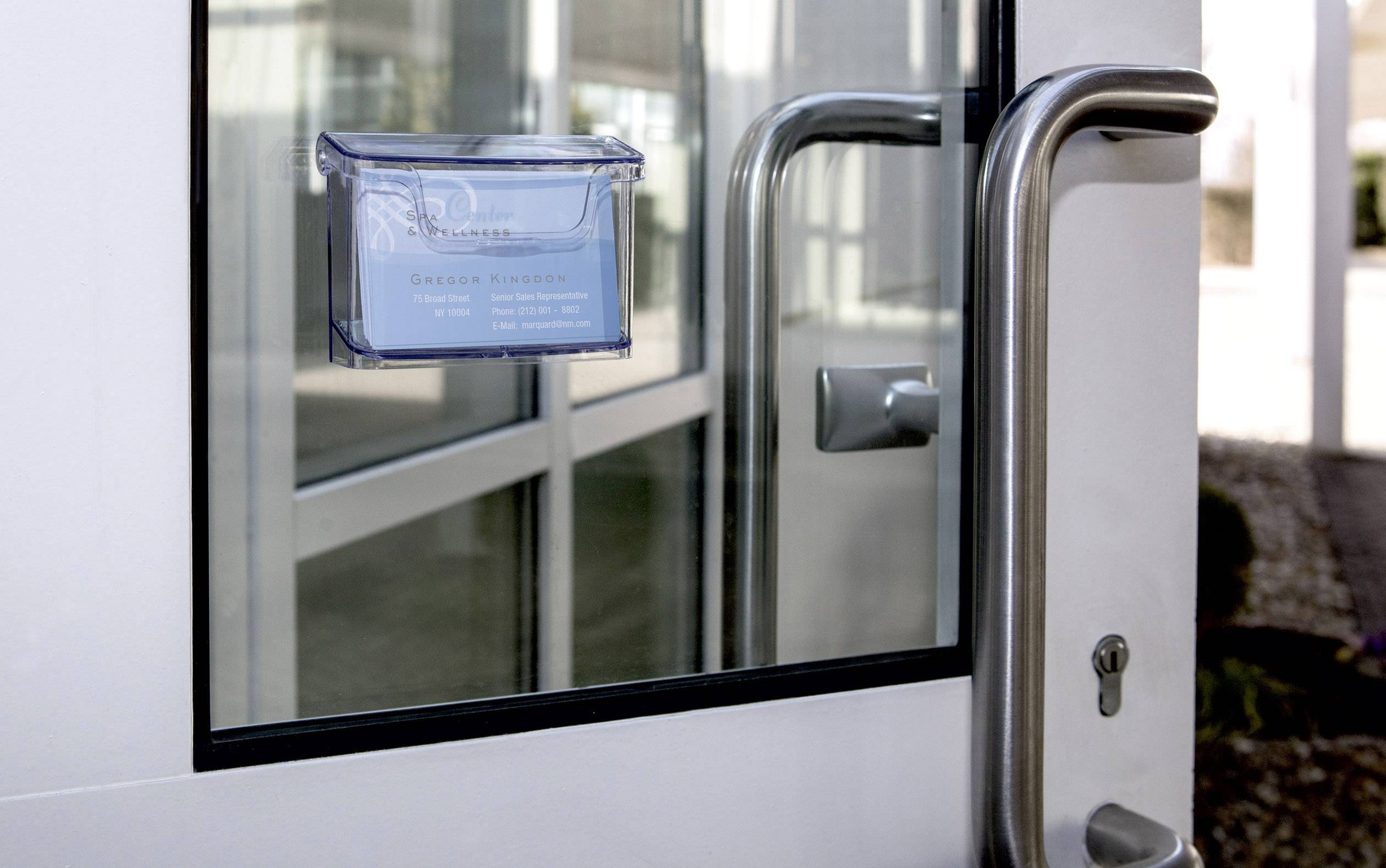 Glastür mit Metallgriff, daneben ist eine Glasscheibe mit einem blauen Schild, das Kontaktinformationen zeigt.