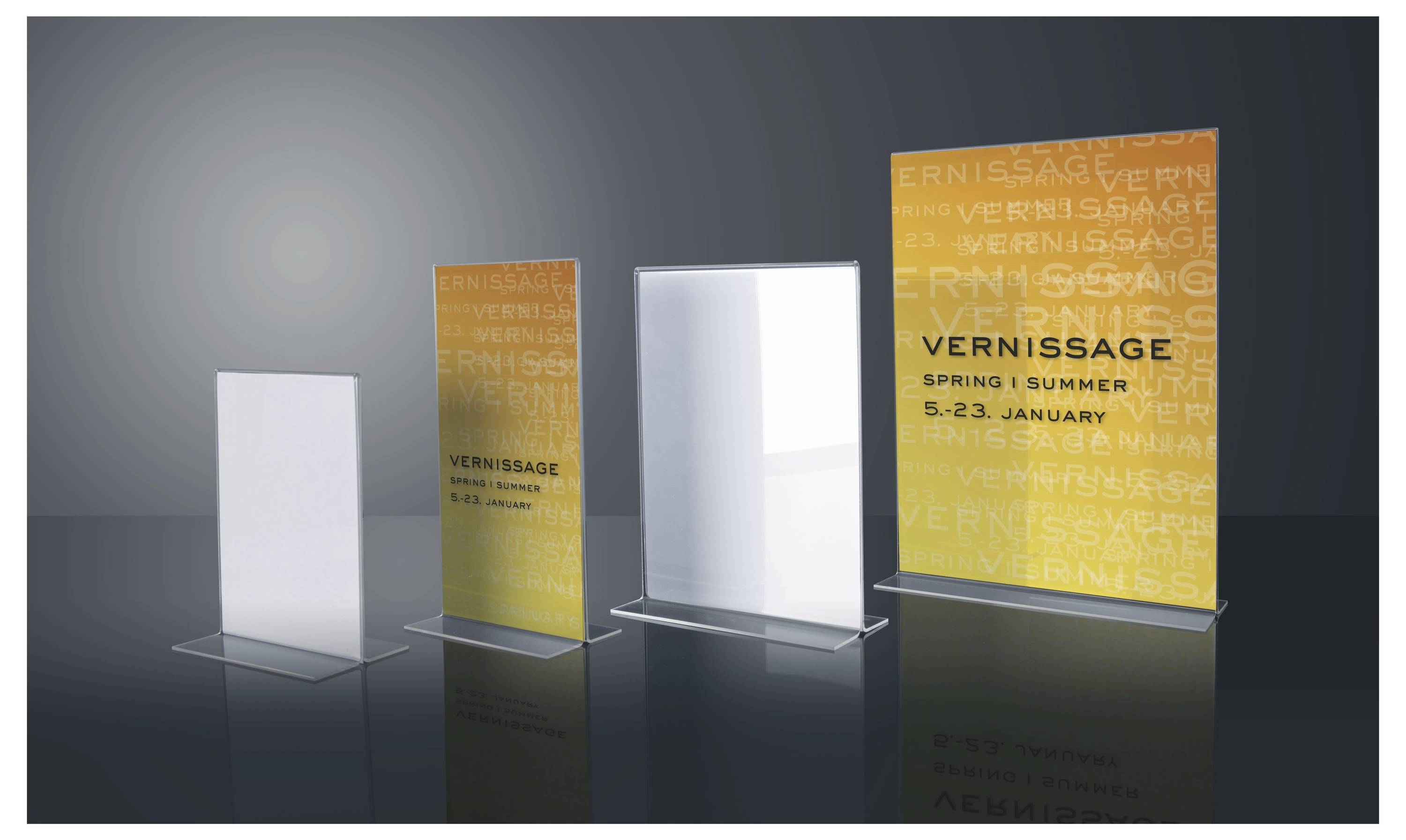 Vier aufrechte Displayschilder auf durchsichtigen Sockeln, darunter zwei leuchtend gelbe „VERNISSAGE"-Plakate und zwei leere weiße Paneele auf dunklem Hintergrund.