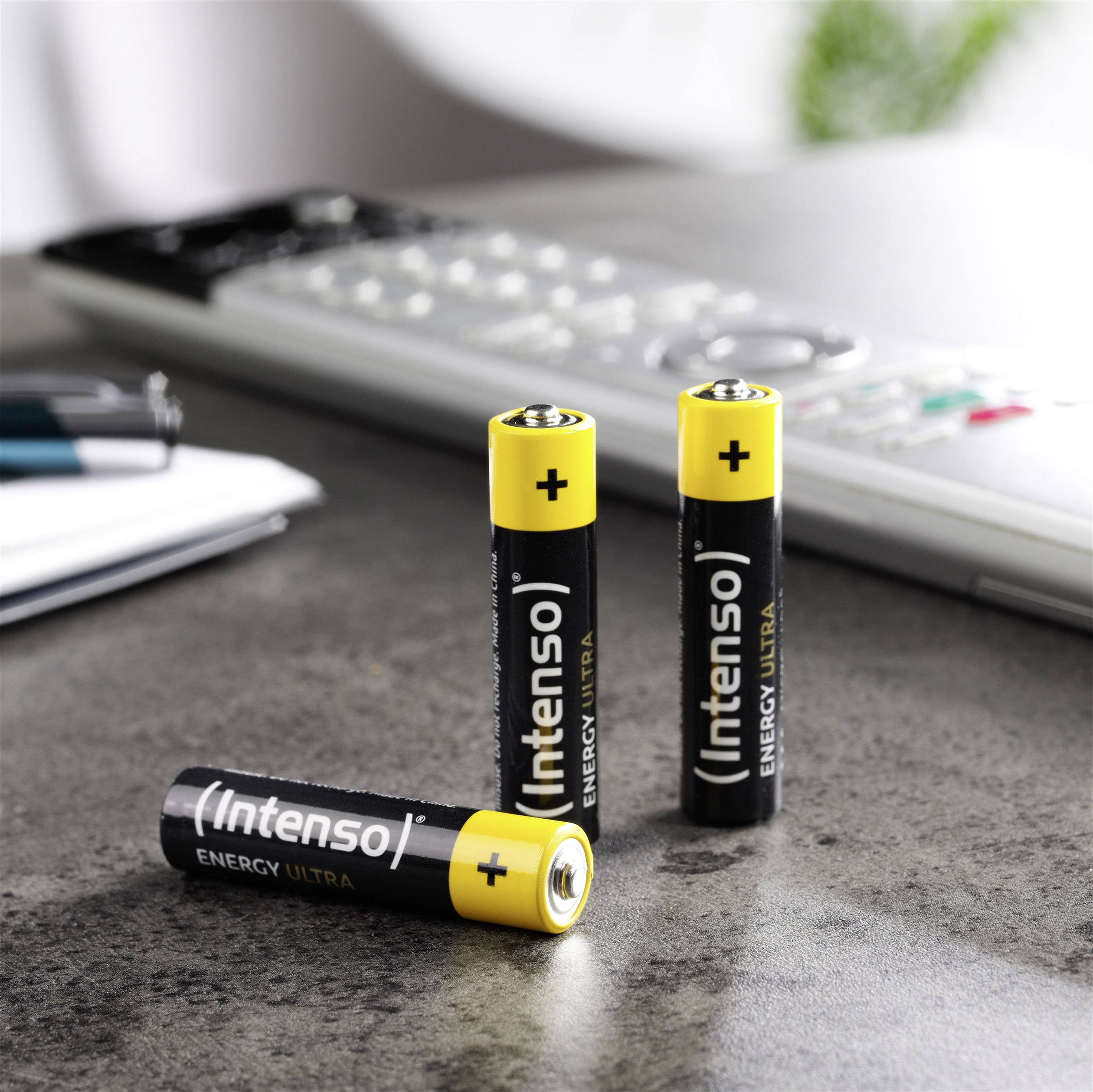 Drei schwarze AA-Batterien mit gelber Oberseite und der Aufschrift 'Intenso Energy Ultra' stehen auf einem Tisch neben einem Taschenrechner.