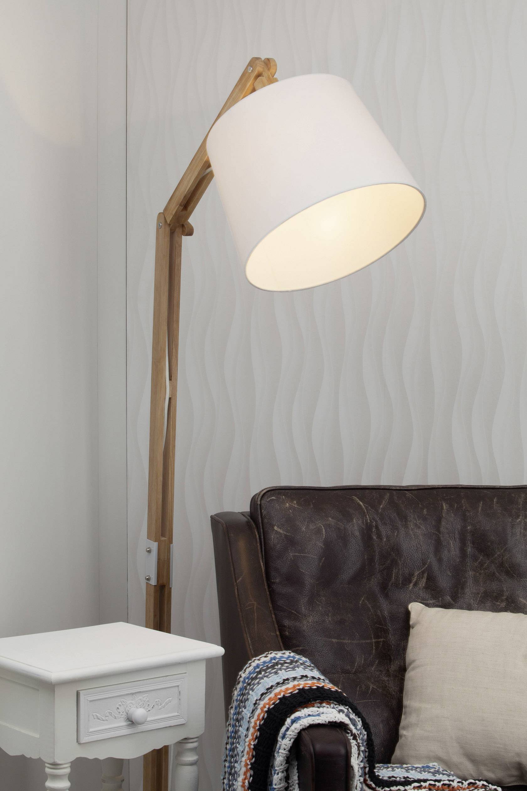 Stehlampe aus Holz neben einem braunen Ledersessel und einem weißen Beistelltisch; gemütliches Wohnraum-Ambiente.