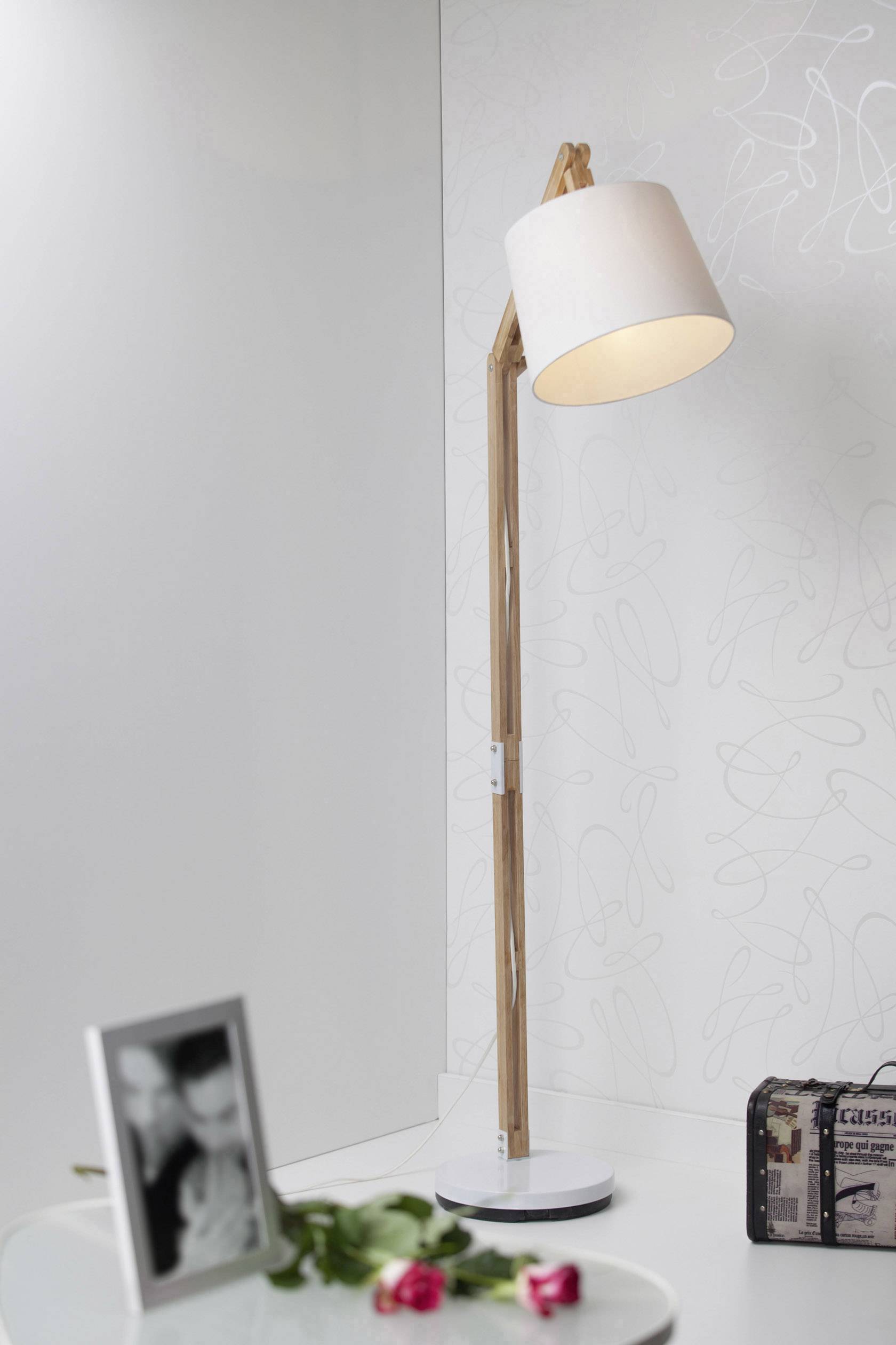 Stehlampe mit Holzständer und weißem Lampenschirm in einem modernen Wohnzimmer. Im Vordergrund ein Tisch mit Rosen und unscharfem Foto.