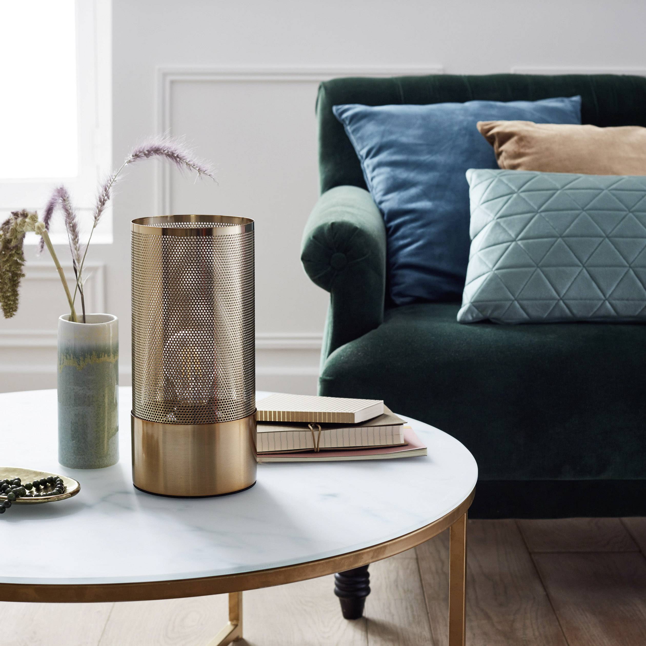 Ein stilvoll eingerichtetes Wohnzimmer mit einem grünen Sofa, dekorativen Kissen und einem runden Marmortisch mit Deko-Elementen.