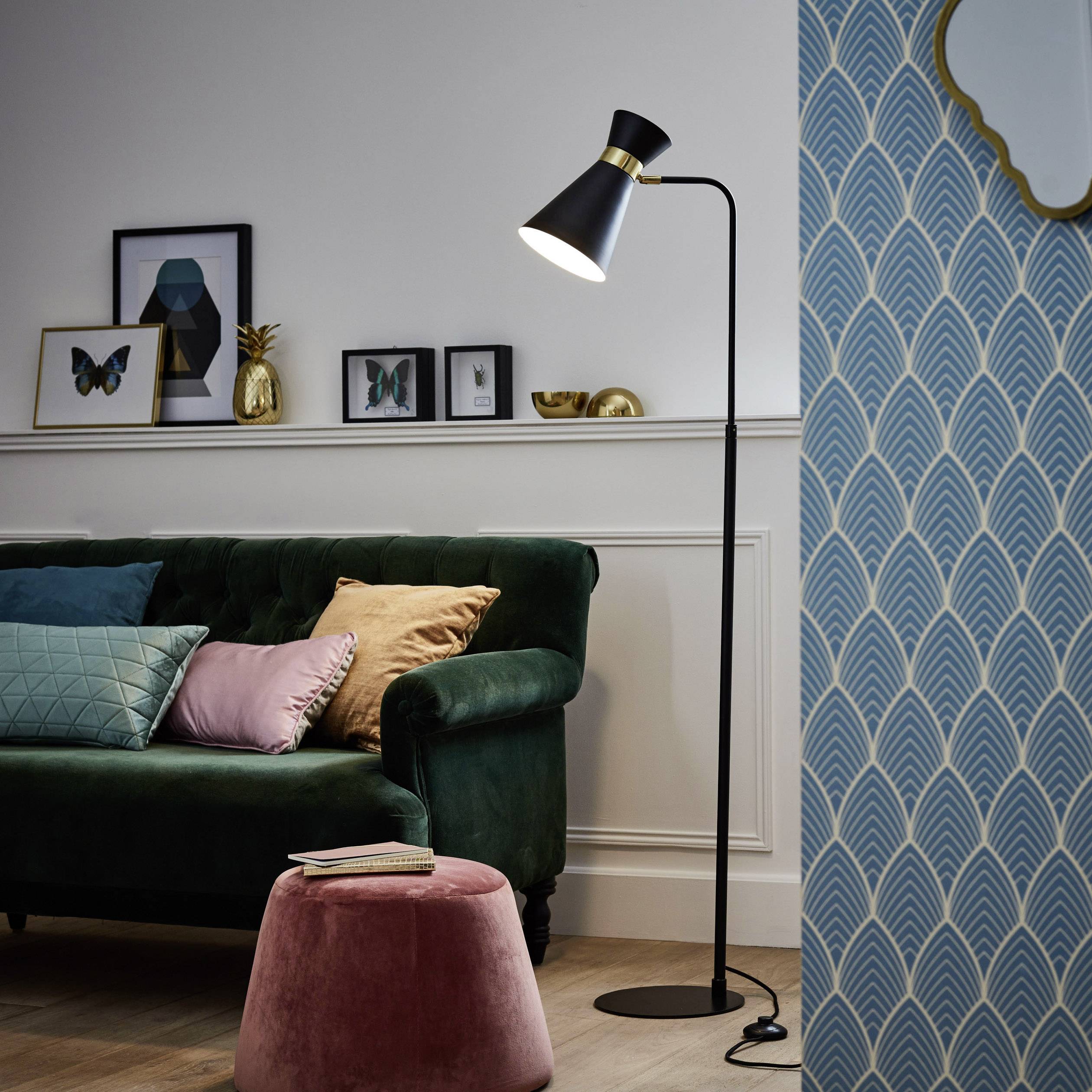 Ein stilvoll eingerichtetes Wohnzimmer mit dunkelgrünem Sofa, pastellfarbenen Kissen, Stehlampe und Bilderrahmen auf einer Ablage.