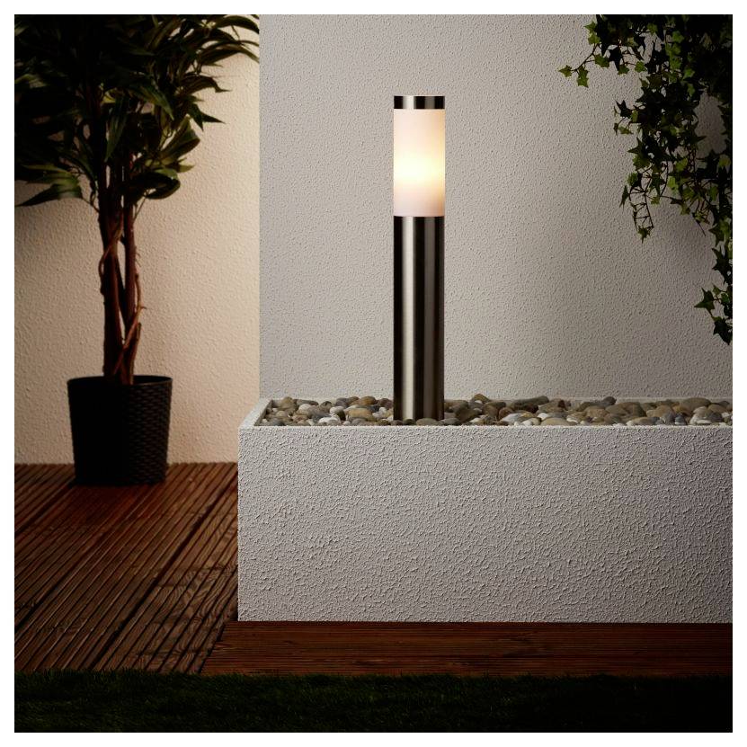 Eine moderne Außenleuchte mit einem zylindrischen Metallsockel und weichem weißem Licht auf einer kieselbefüllten Plattform, neben einer Topfpflanze.