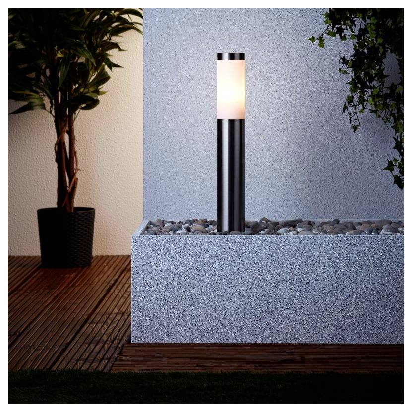 Eine moderne Außengartenleuchte mit elegantem Metalldesign steht beleuchtet in einer kieselbelegten Ecke neben einer Topfpflanze unter sanftem Licht.