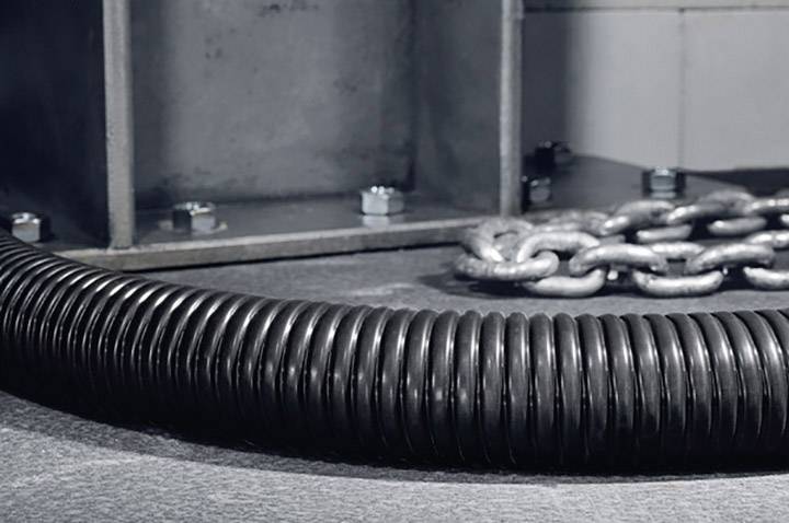 Gerollter schwarzer Kabelschutzschlauch liegt neben einer schweren Metallkette auf einem grauen Boden, im Hintergrund Metallstruktur.